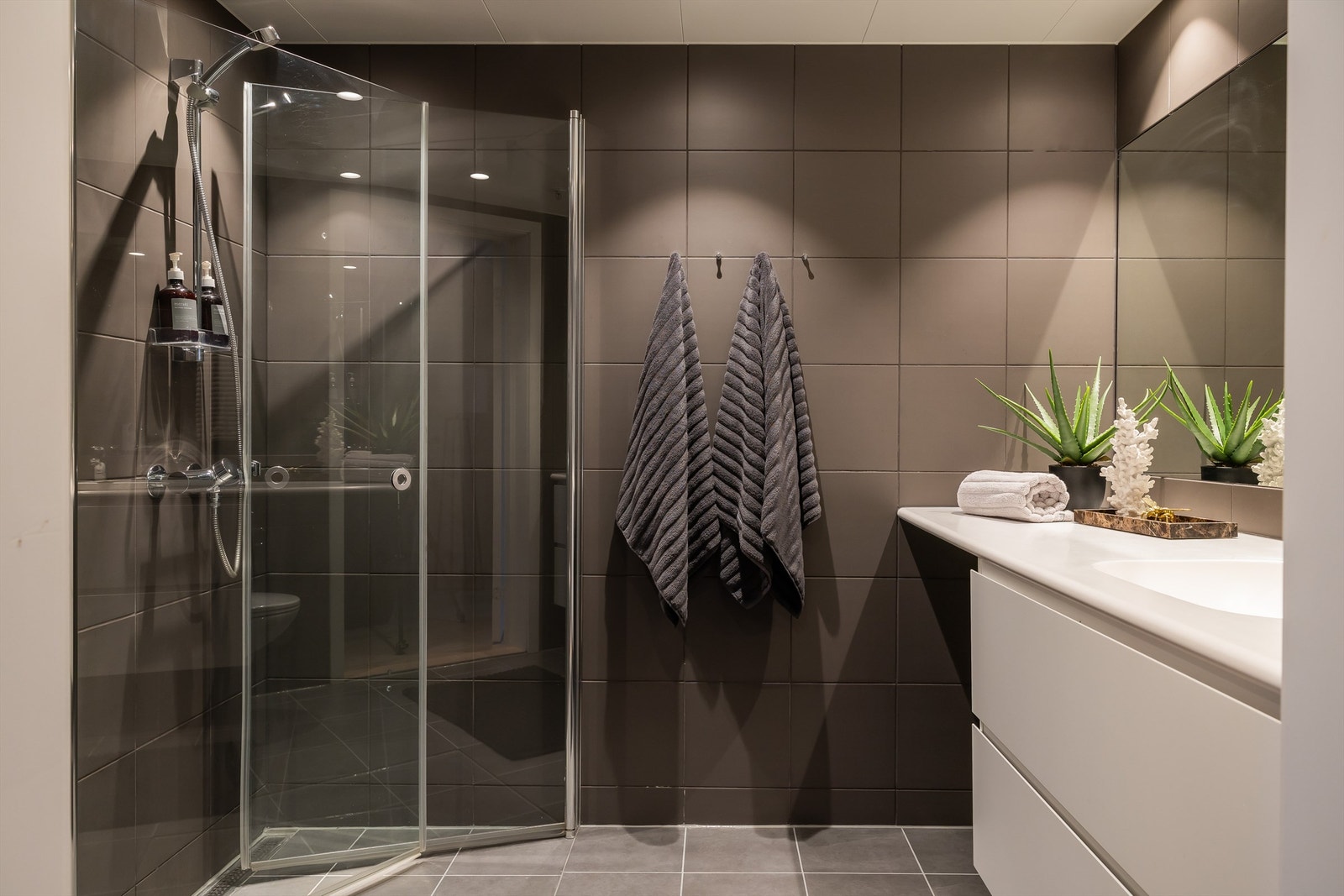 Praktisk dusjhjørne, vegghengt toalett og servant med skuffeseksjon. Galleribilde