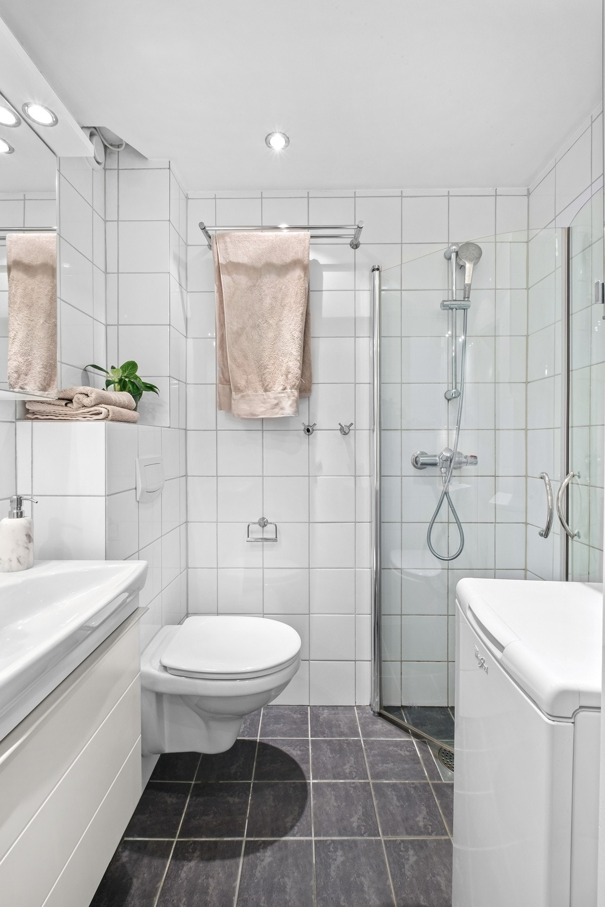 Lyse fliser på vegger, mørkt flislagt gulv med varmekabler og himlingen er bestående av malte flater og spotlights. Galleribilde