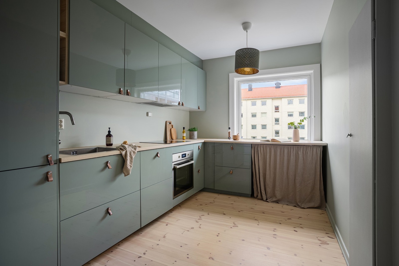 Kjøkken med moderne innredning, grønne fronter. Store vinduer sikrer dagslys, god plass til spisegruppe Galleribilde