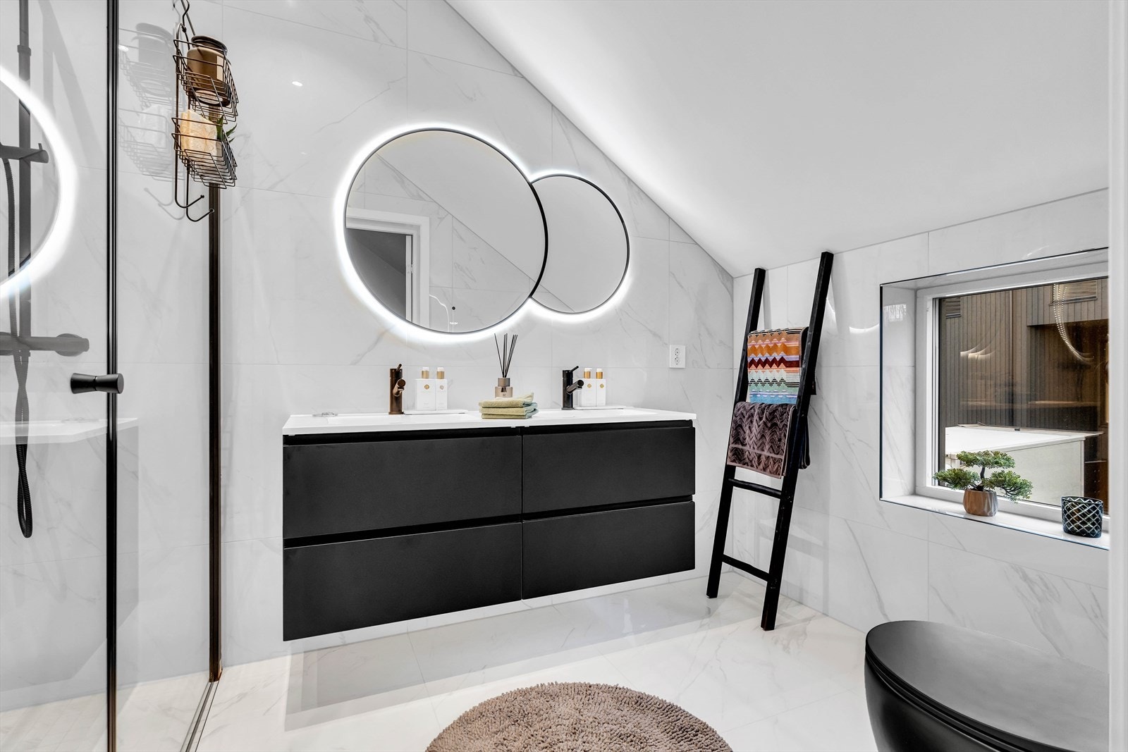 Neste bad har marmorinspirerte fliser, vindu som gir godt med lys, god takhøyde, flott innredning, dobbelt runde speil med belysning og detaljer i sort. Galleribilde