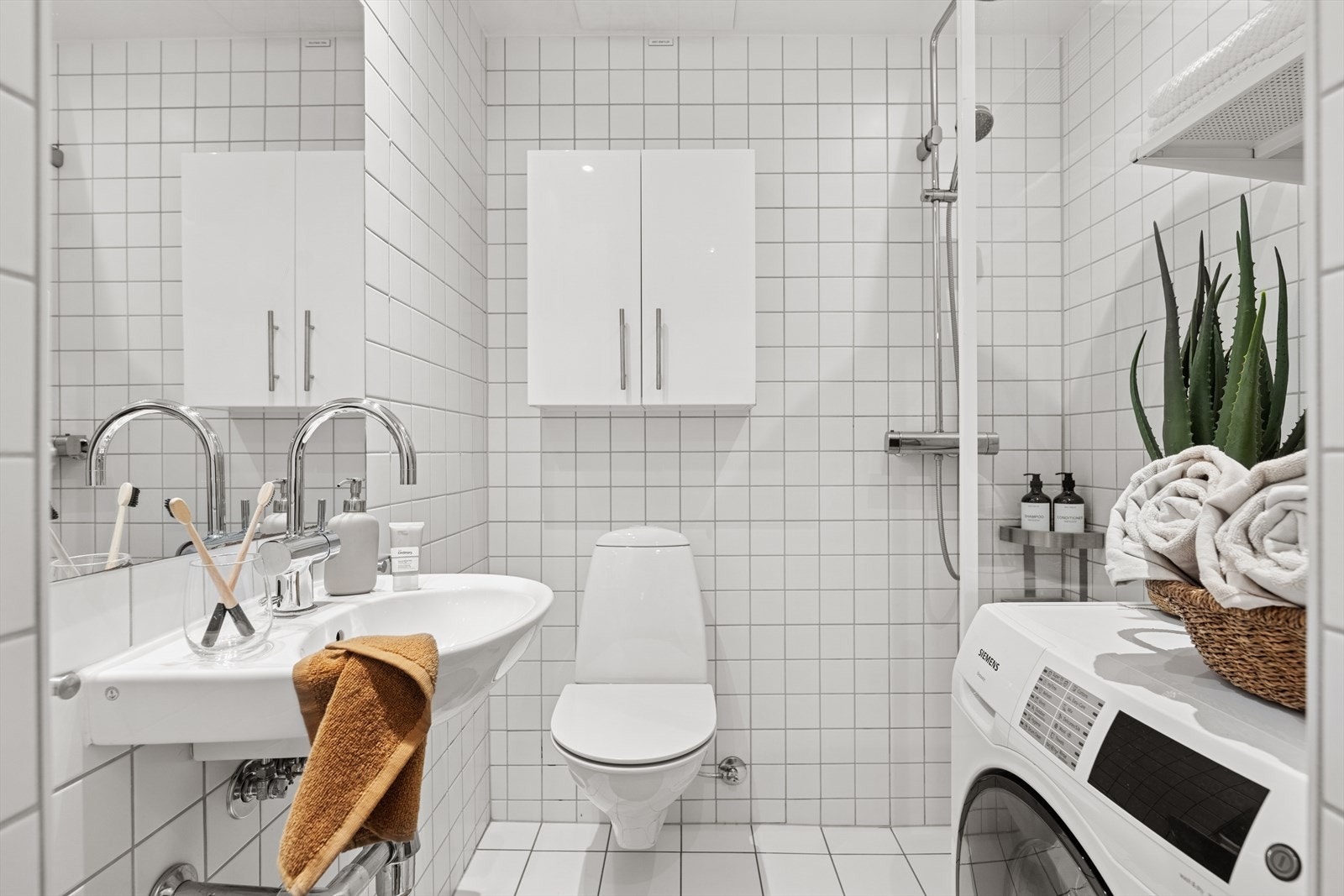 Flislagt baderom med varmekabler i gulvet, skapplass og opplegg for vaskemaskin. Galleribilde