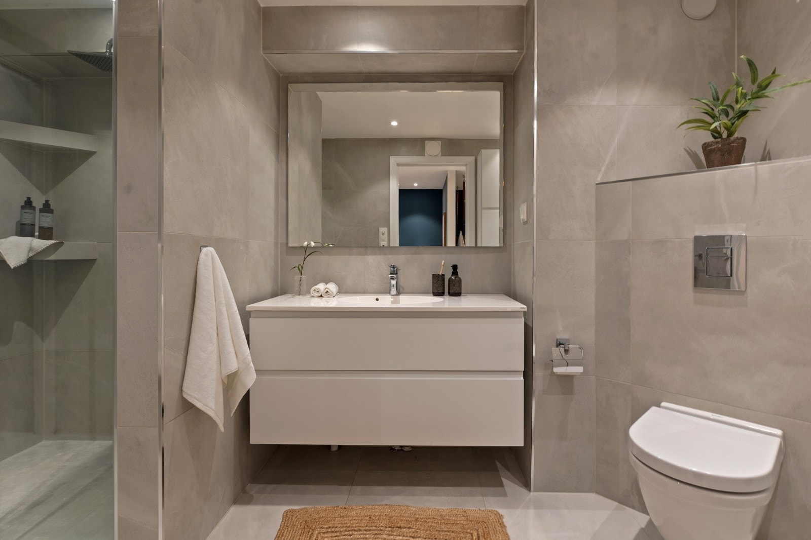 Baderommet fremstår strøkent med lysegrå fliser på gulver og vegger Galleribilde