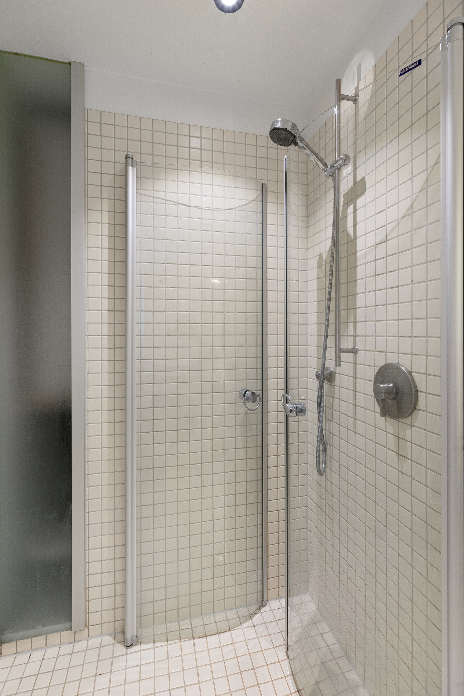 Dusjhjørne med svingdører i glass og innebygd dusjarmatur, samt veggmontert toalett. Galleribilde