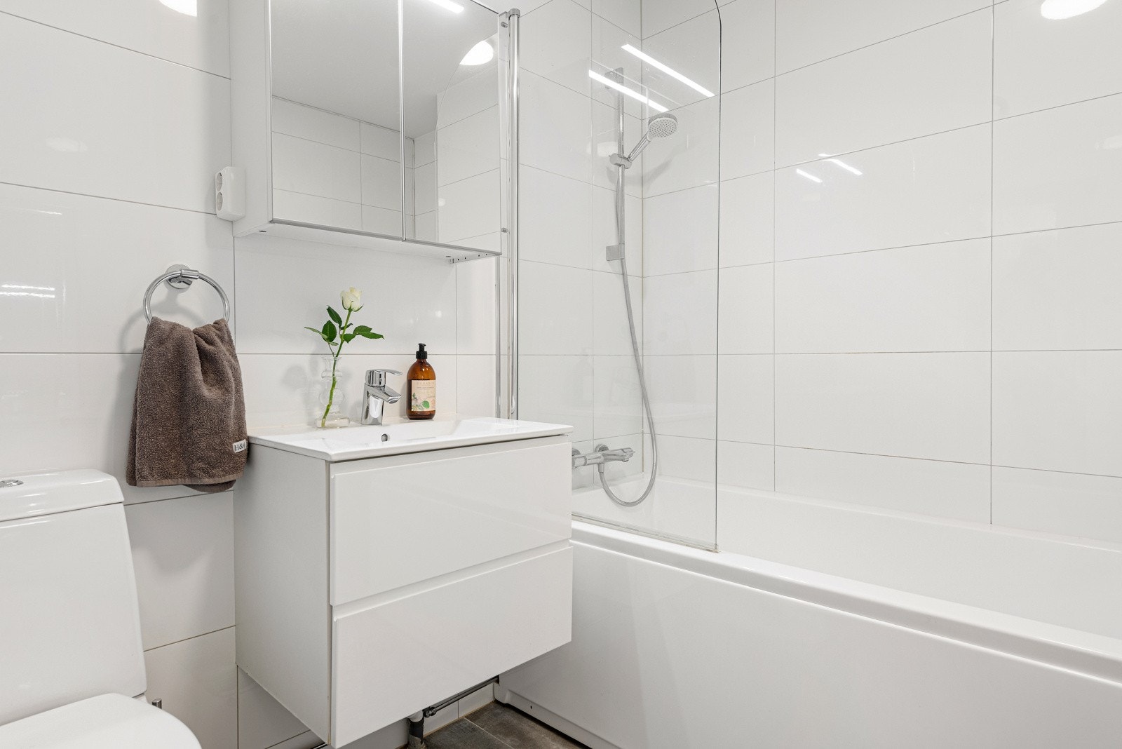 Badekar med vegghengt dusjarmatur og glassdør. WC. Speilskap med overlys og stikkontakt over servant Galleribilde