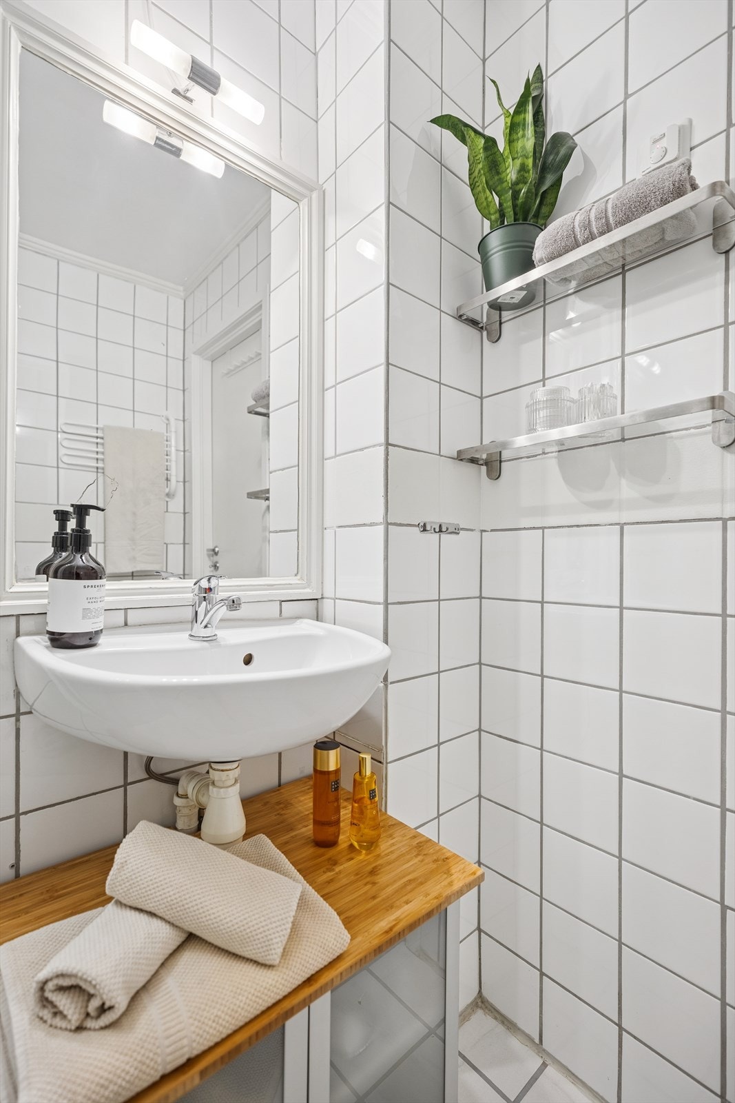 Innredning består av vegghengt servant med underskap og speil med belysning på veggen over servant, gulvmontert toalett, speilskap og et dusjkabinett. Galleribilde