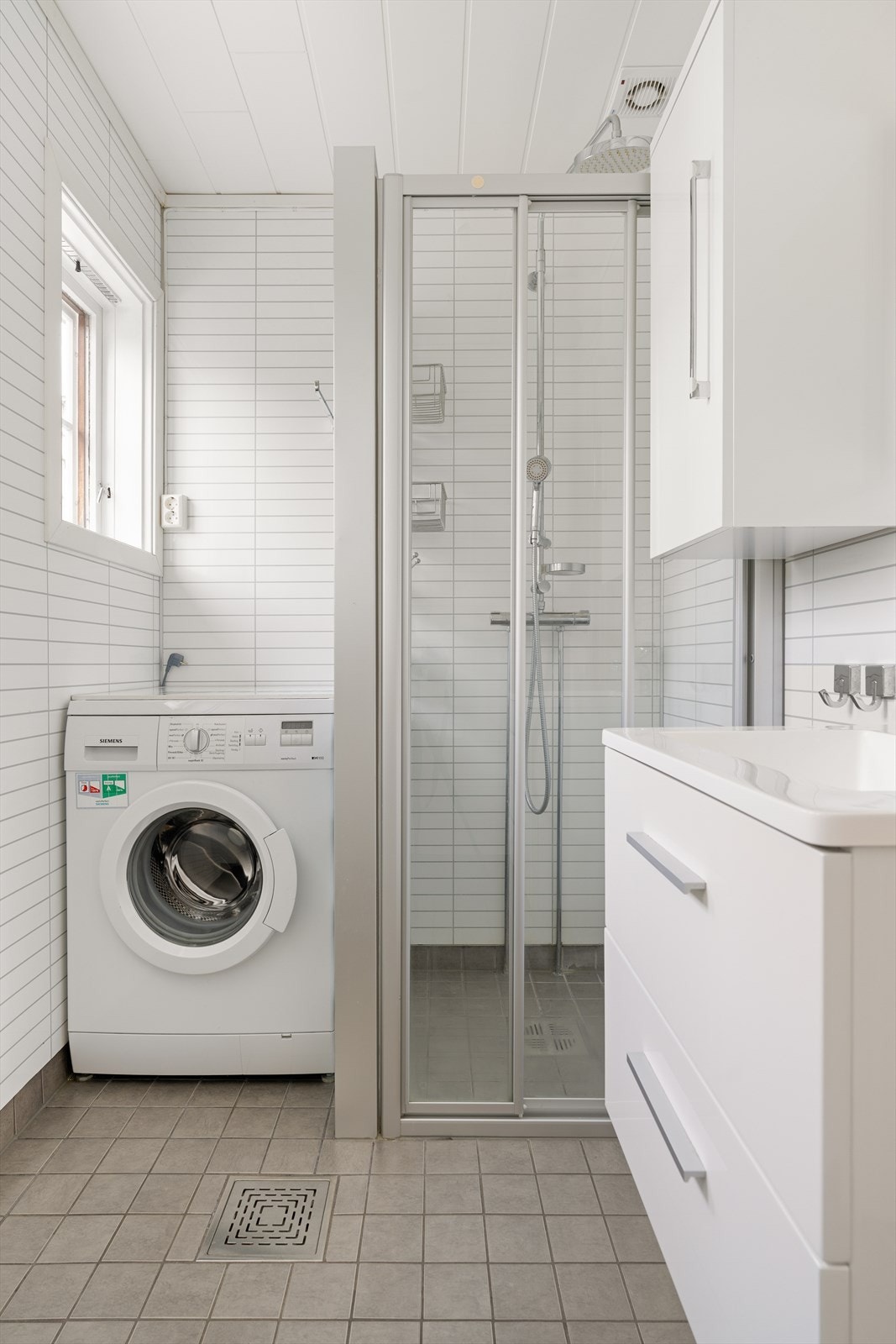 Videre er badet utstyrt med servantskap med speil og sideskap, dusjhjørne med regndusj og vegghengt toalett. Galleribilde