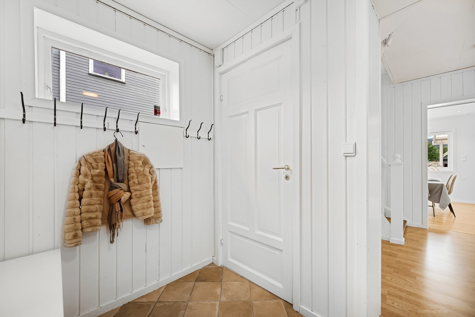 Boligen har en lys entré med fliser på gulv og panel på vegger. Det er garderobeskap i entréen. Galleribilde