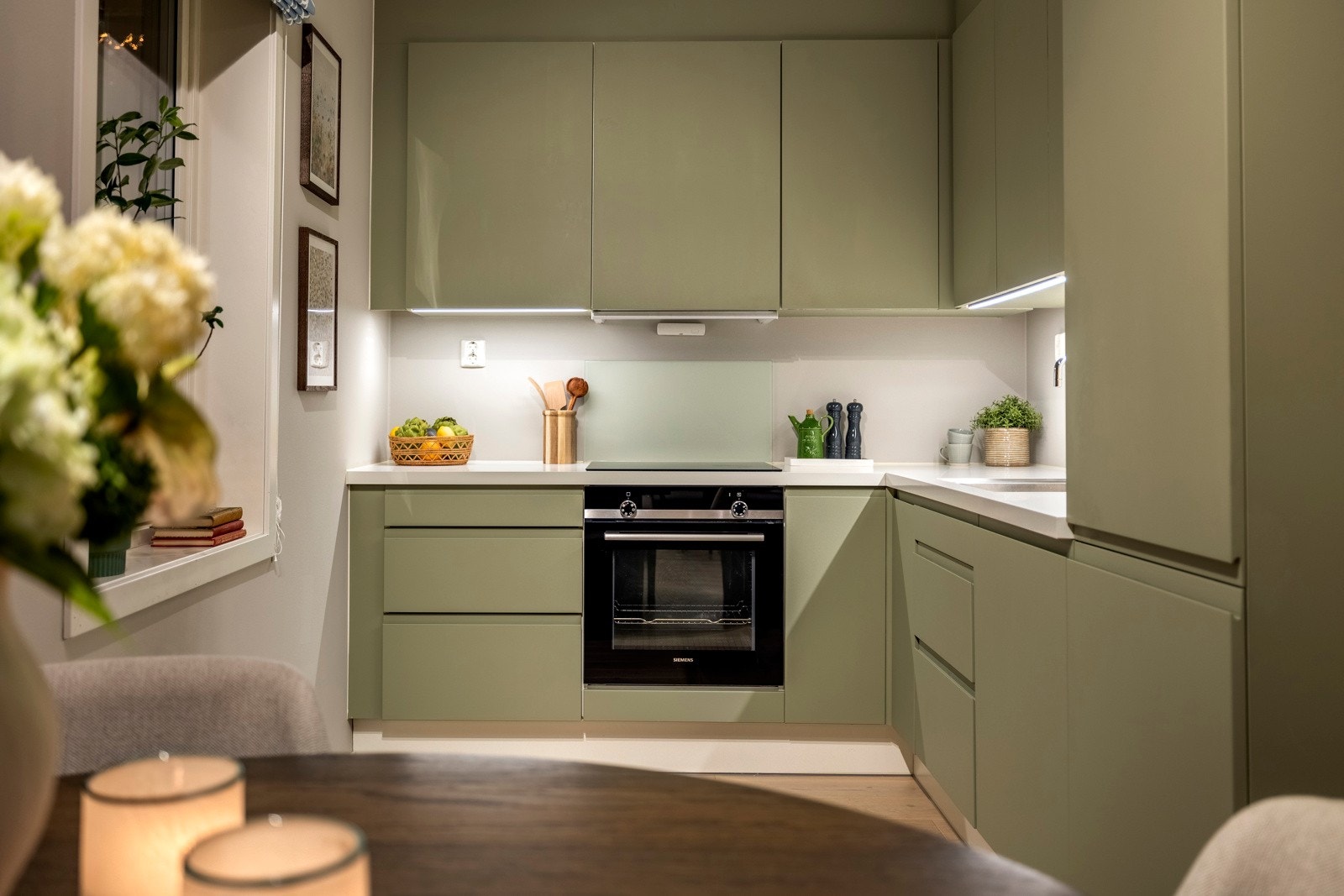 Benkeplatene er i lys laminat, og veggen mellom benk og overskap består av malte flater, samt en elegant glassplate over vaskekum og stekeplate. Galleribilde