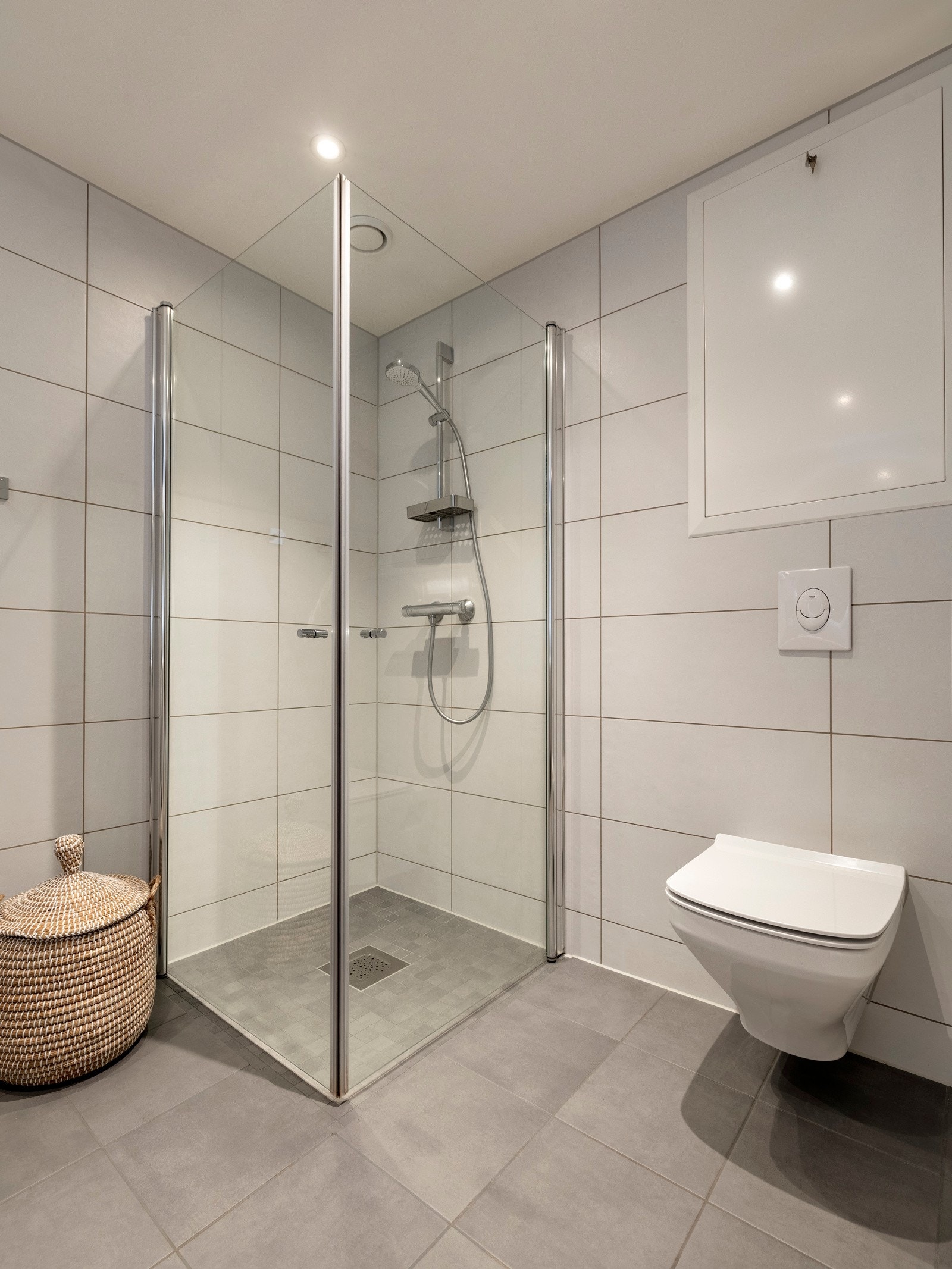 Bak innfellbare glassdører finner man et nedsenket dusjhjørne, hvor dusjgarnityret er elegant montert på veggen. I tillegg har badet et vegghengt toalett og opplegg for vaskemaskin og tørketrommel. Galleribilde