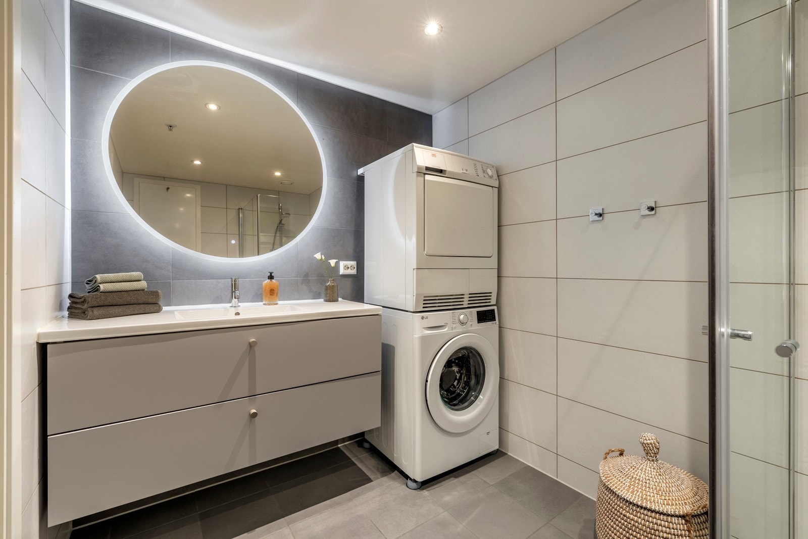 Baderommet er elegant innredet med lysegrå gulvfliser og mørkegrå fliser vegger, som skaper en flott kontrast. Himlingen er stilfullt belyst med downlights, og det er behagelig vannbåren gulvvarme som gir ekstra komfort. Galleribilde