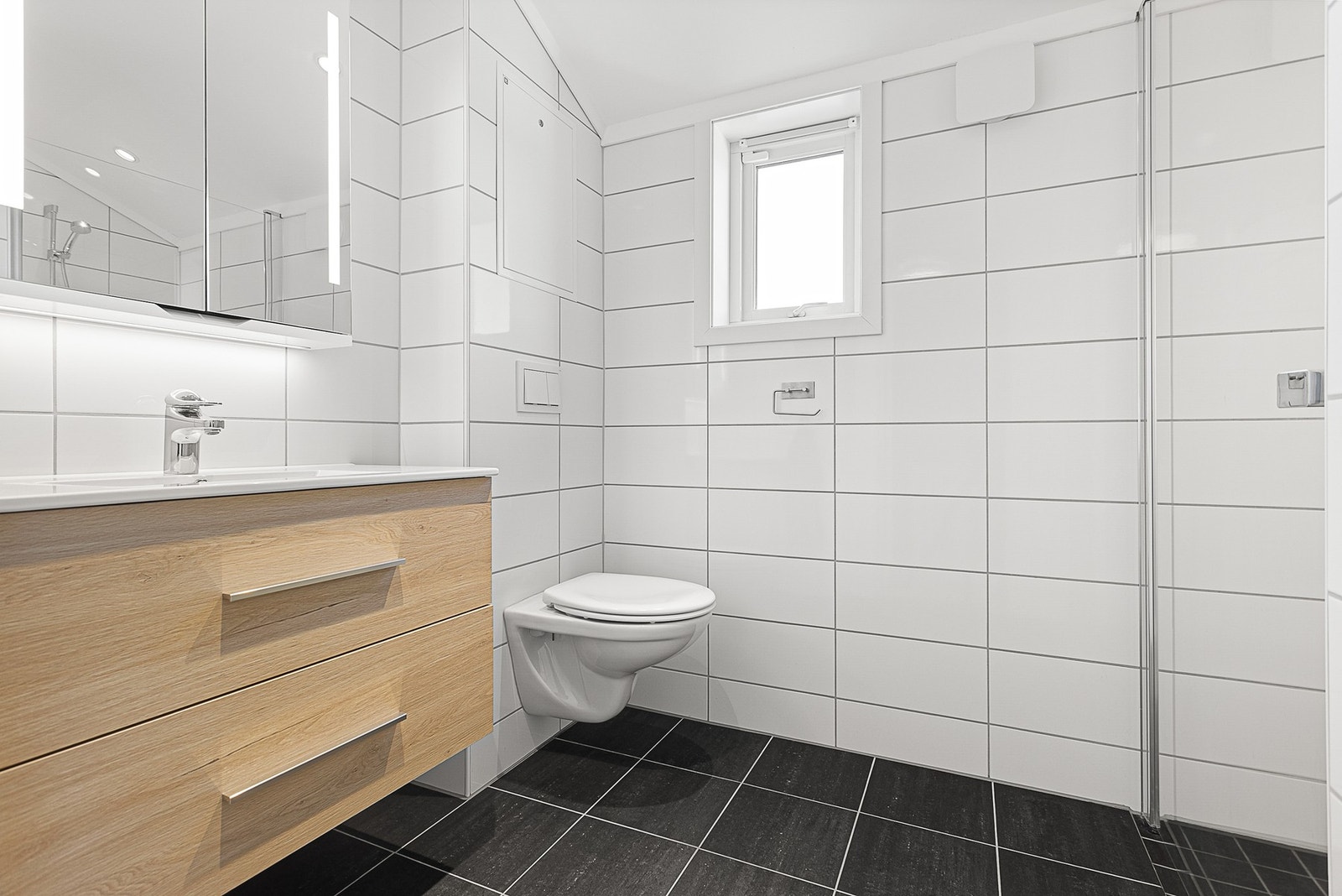 Baderom med flislagte overflater. Veggmontert toalett, innredning med servant og dusjhjørne med glassdører Galleribilde
