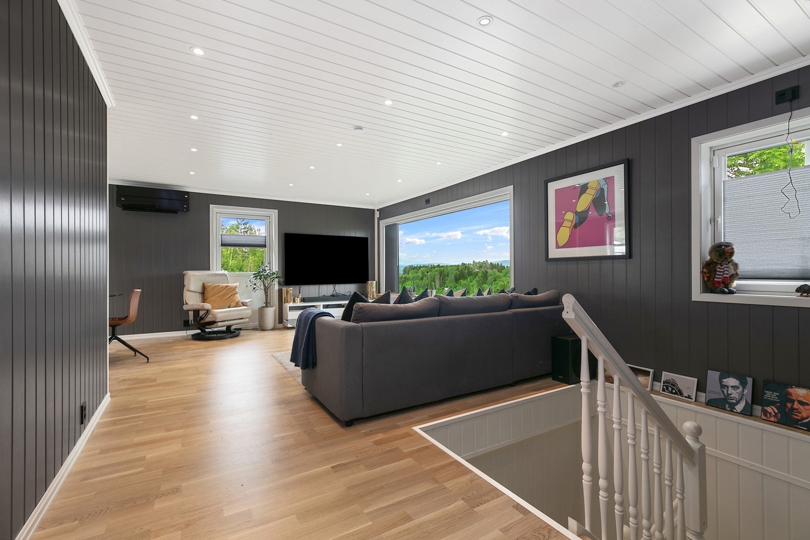 Innbydende stue med pene overflater med parkett på gulv, malt panel på vegg i en mørkere grå tone og utstrakt bruk av downlights i himling, som gir et moderne uttrykk. Galleribilde