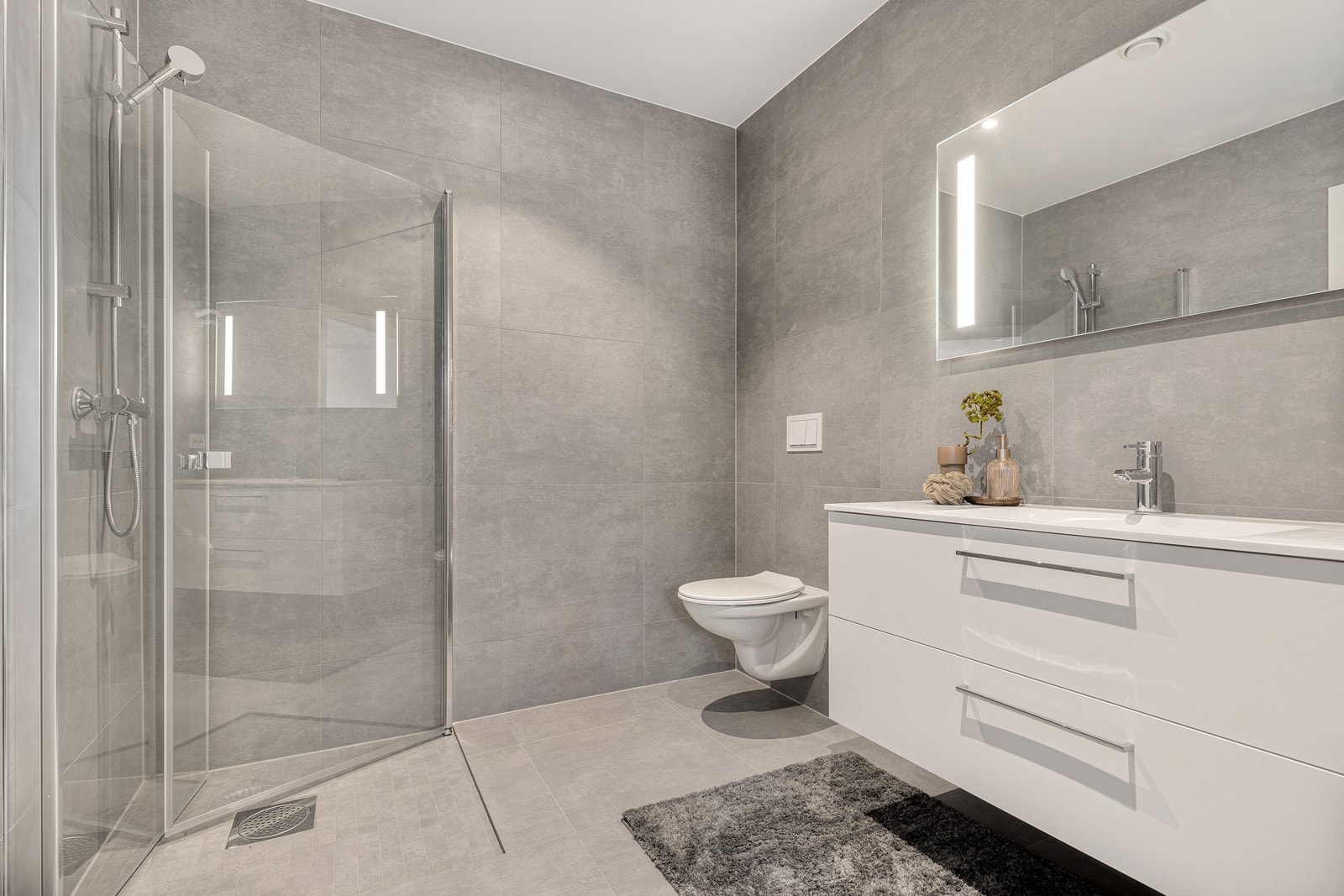 Eget bad med lekre fliser på vegger og gulv. Innredet med vegghengt servant, vegghengt toalett og dusjhjørne med innefellbare dører Galleribilde