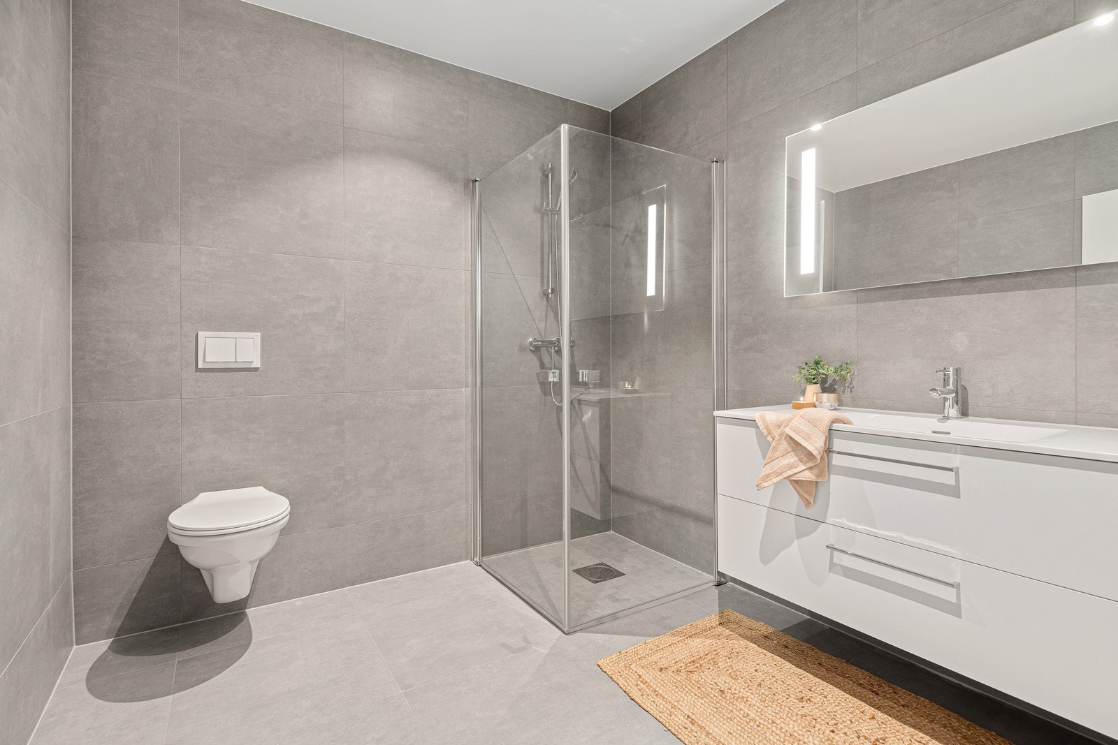 Lekkert bad med store fliser på vegger og gulv. Stor servant med skuffesystem og dusjhjørne med innfellbare dører Galleribilde