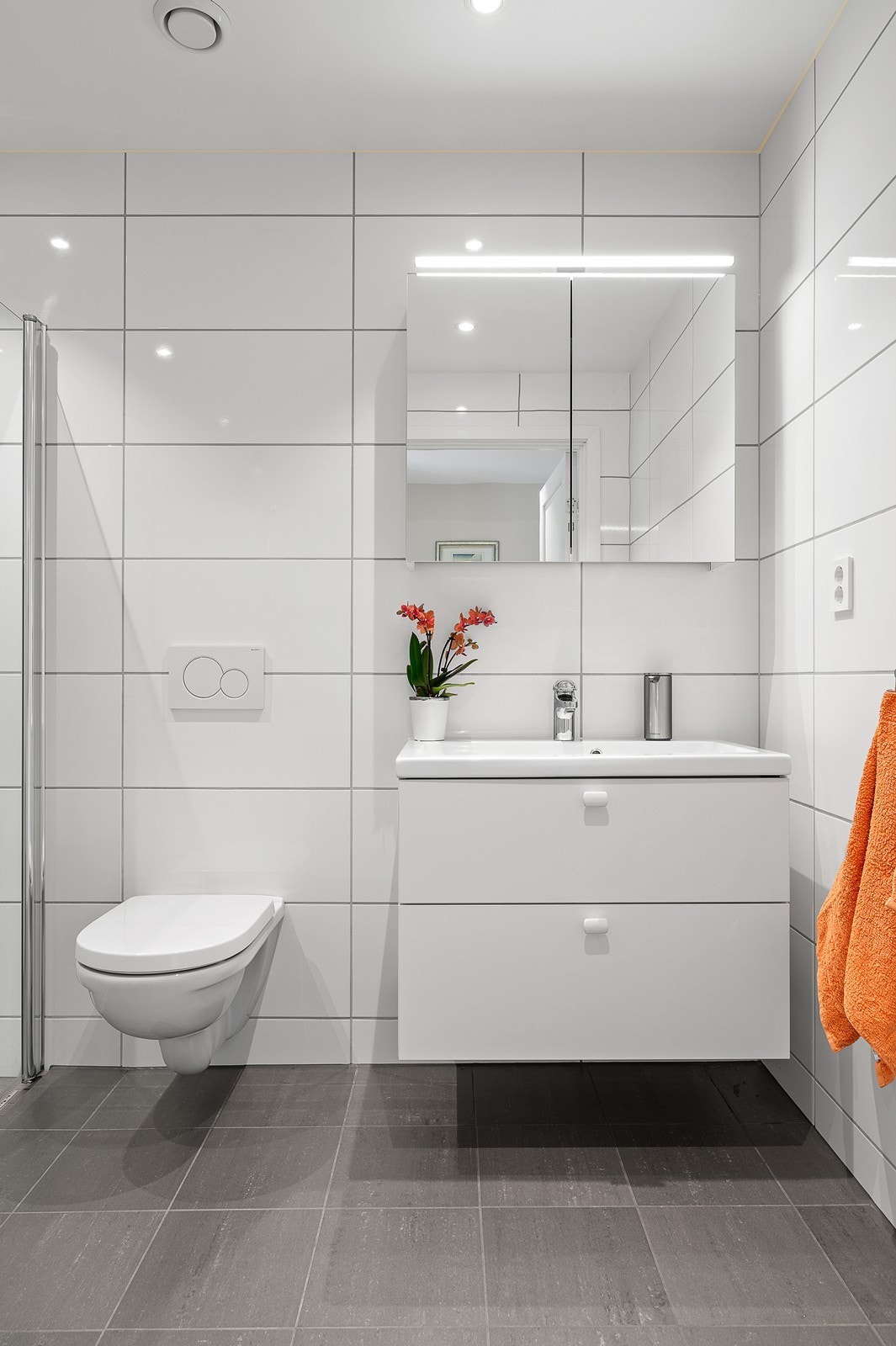 Badet er innredet med dusjhjørne, vegghengt toalett og servant i innredning Galleribilde