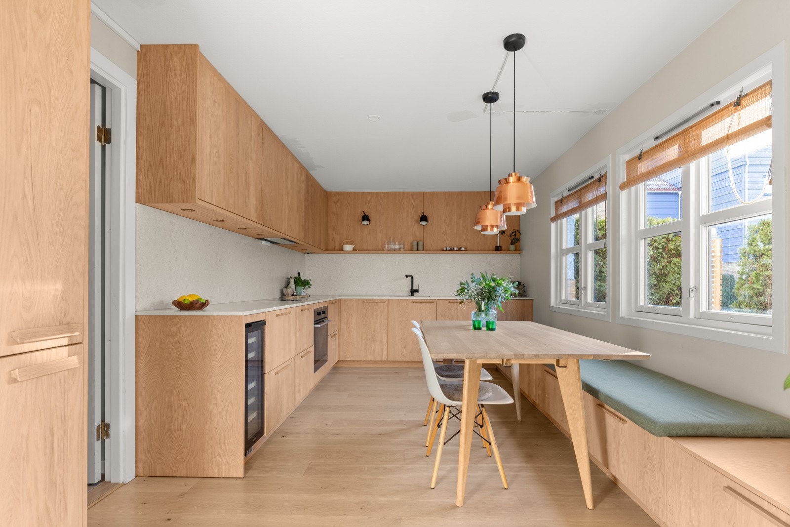 En spesialtilpasset sittebenk langs den ene langveggen skaper en sosial og praktisk spiseplass, perfekt integrert i kjøkkenets design. Galleribilde