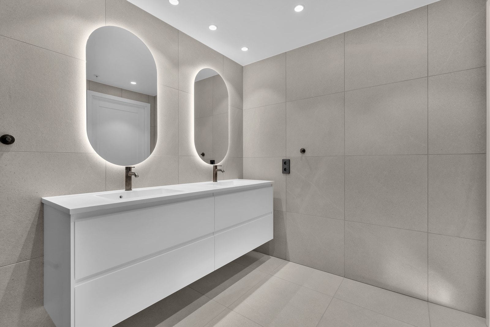 Begge badene har stor fliser på gulv og vegger. Bedene har god belysning fra spotter i tak og lys i speil. Galleribilde