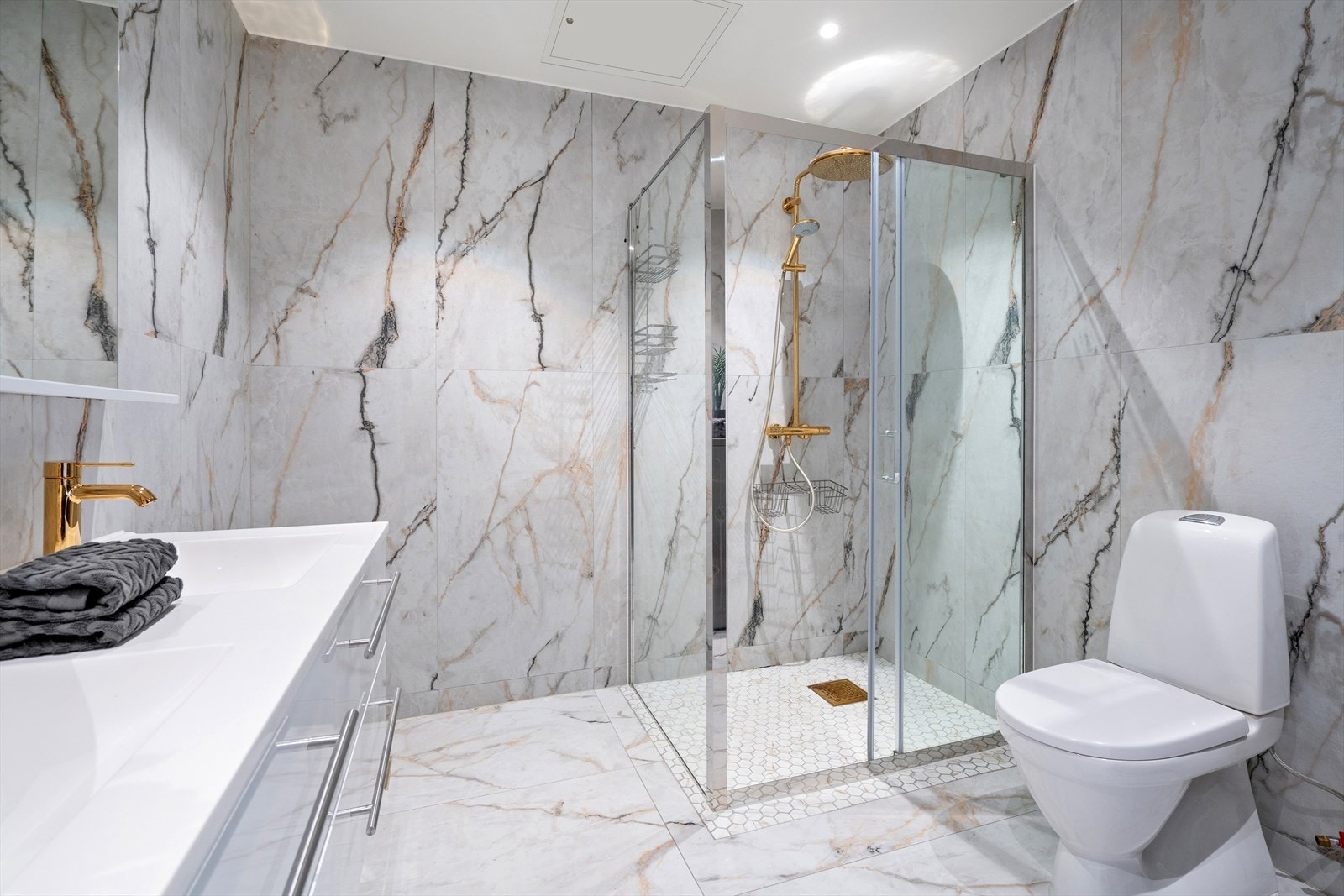 Baderomsinnredningen består av toalett, romslig dusj med skyvbare glassdører, dobbel servant nedfelt i innredning og speil på vegg. Galleribilde