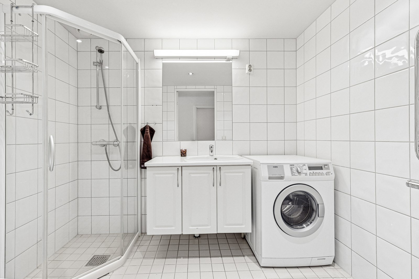 Badet har hvite fliser på veggene og gulvet. Det er opplegg for vaskemaskin. Galleribilde