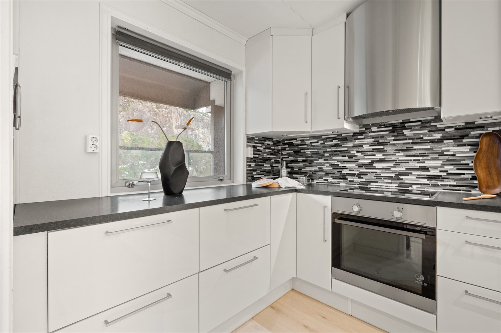 Kjøkkeninnredning med slette fronter og laminat benkeplate. Over benkeplaten er det benyttet fliser, stål oppvaskkum og ventilator. Galleribilde