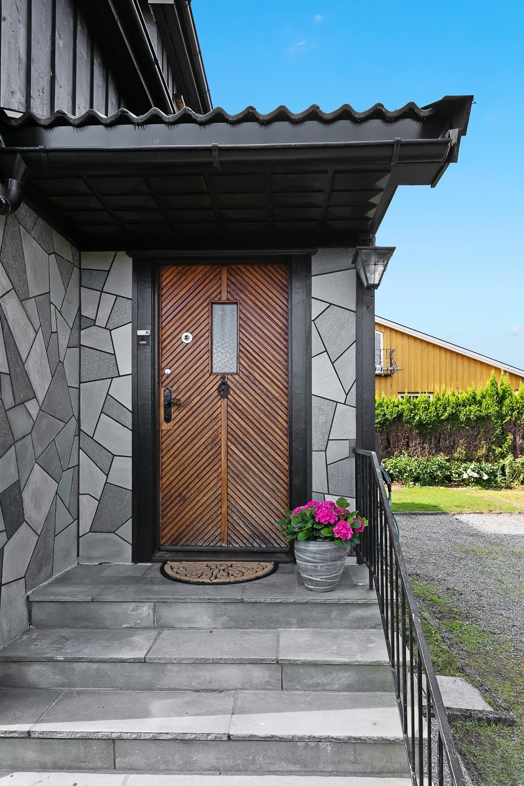 Inngangspartiet er overbygd og har trapp med betongheller og smijernsrekkverk. Galleribilde