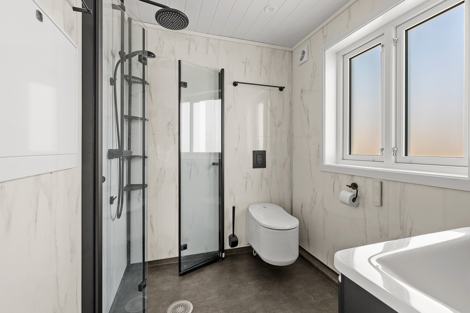 Flott bad som er pusset opp i nyere tid. Dusjhjørne har dusjdører med sorte profiler og veggmontert dusjsett med takdusj og hånddusj i sort utførelse. Galleribilde