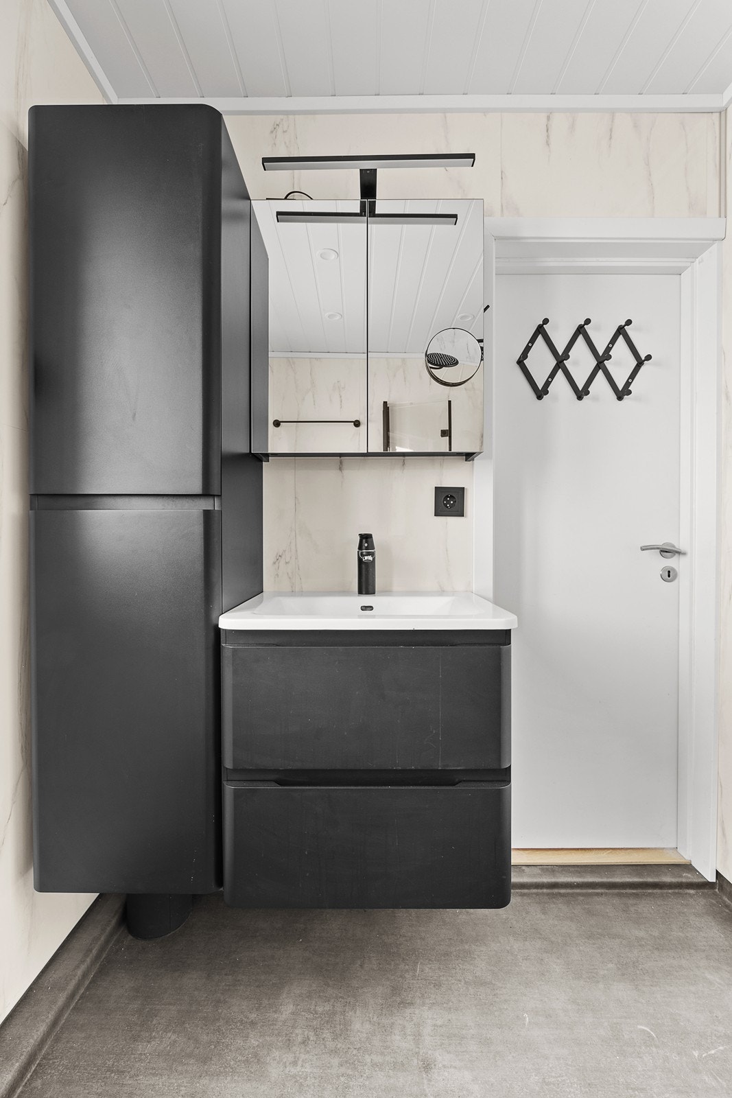 Sort baderomsinnredning med servantskap, vestrehengslet høyskap og vegghengt speilskap med baderomslampe. Galleribilde