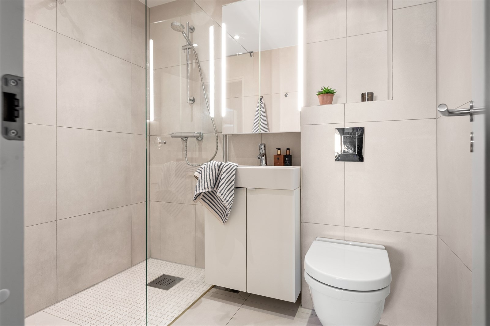 Badet er innredet med servant på vegghengt servantskap, vegghengt toalett med innebygd sisternekasse. Videre er det romslig dusjhjørne med glassvegg. Galleribilde