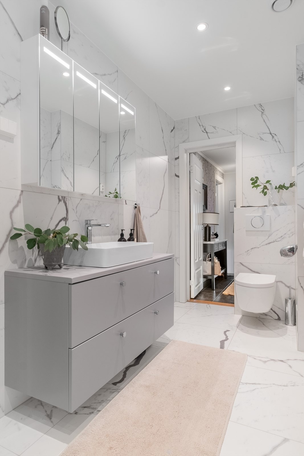 Baderommet er innredet med vegghengt klosett, servant plassert på innredning, speilskap m/lys og dusjhjørne med svingbare glassdører. Galleribilde