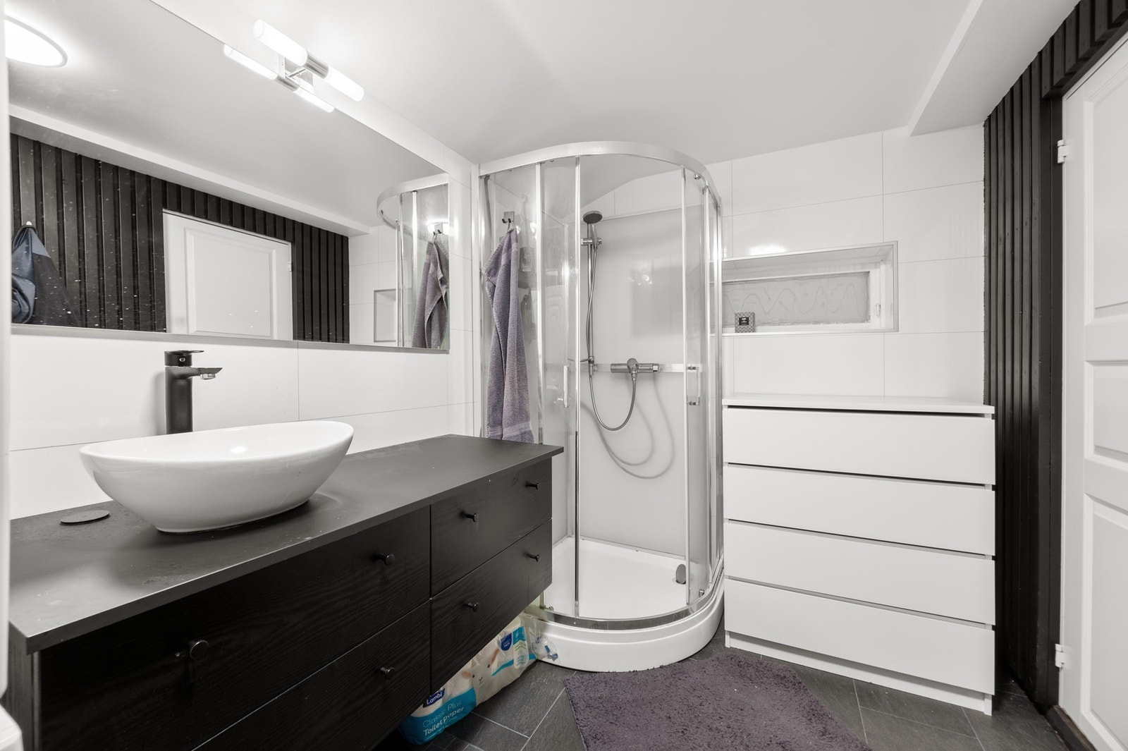 Badet har flislagt gulv med varme og inneholder servantinnredning, dusjkabinett og toalett Galleribilde