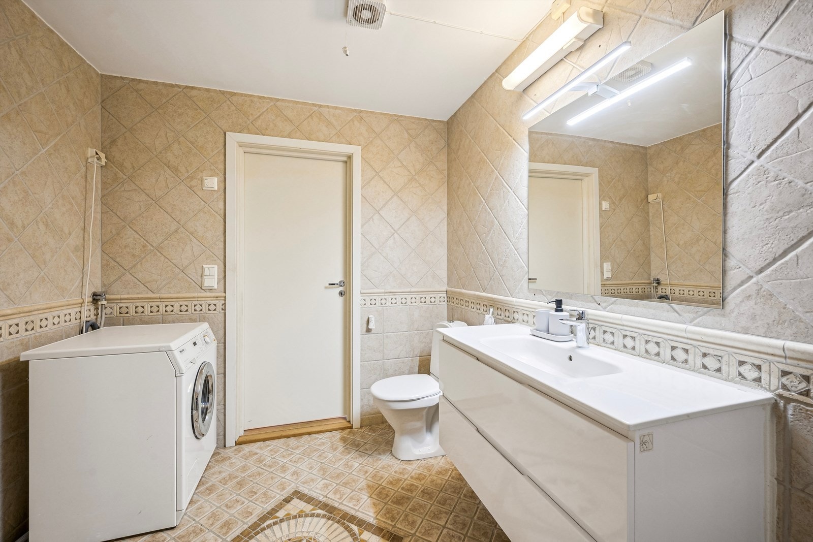 Pent og romslig baderom med moderne servant, fine fliser, toalett og praktisk vaskemaskinplass. Galleribilde