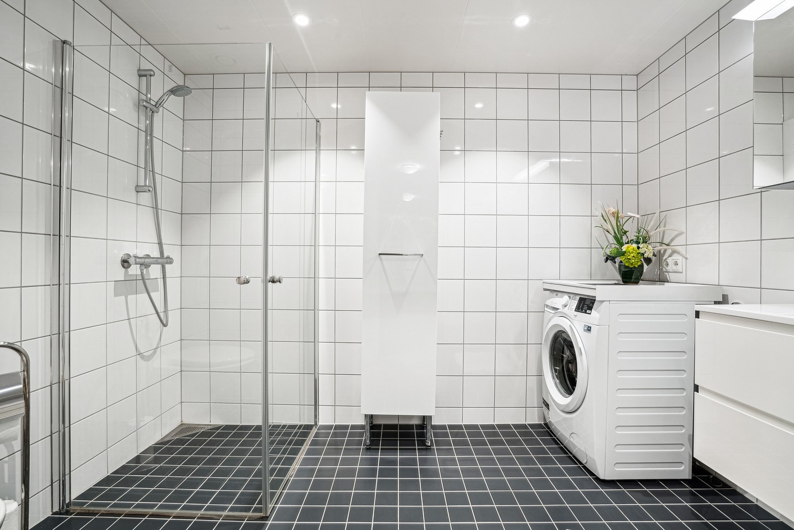 Stort bad med dusjhjørne, opplegg for vaskemaskin, toalett og servant med skuffer. Galleribilde