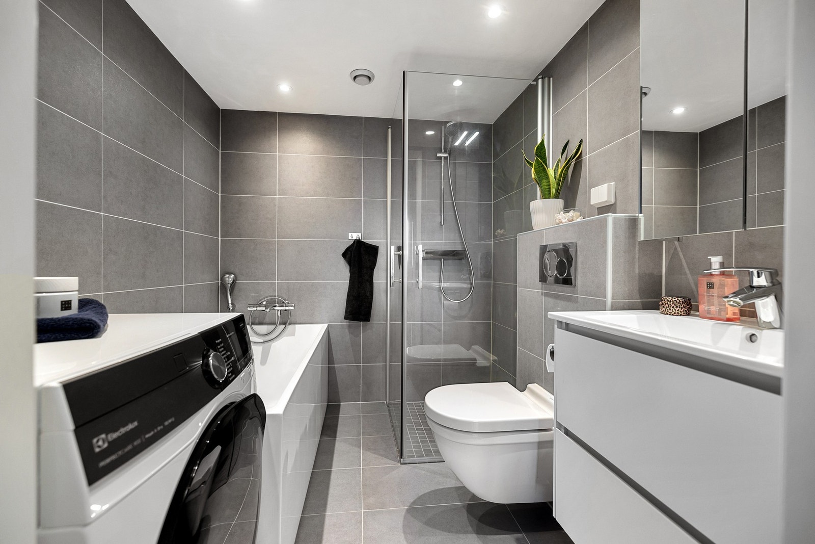 Moderne og stilrent bad fra 2016, med flislagte overflater, gulvvarme og downlights. Praktisk innredet med både dusjhjørne og frittstående badekar, samt opplegg for vaskemaskin. Galleribilde