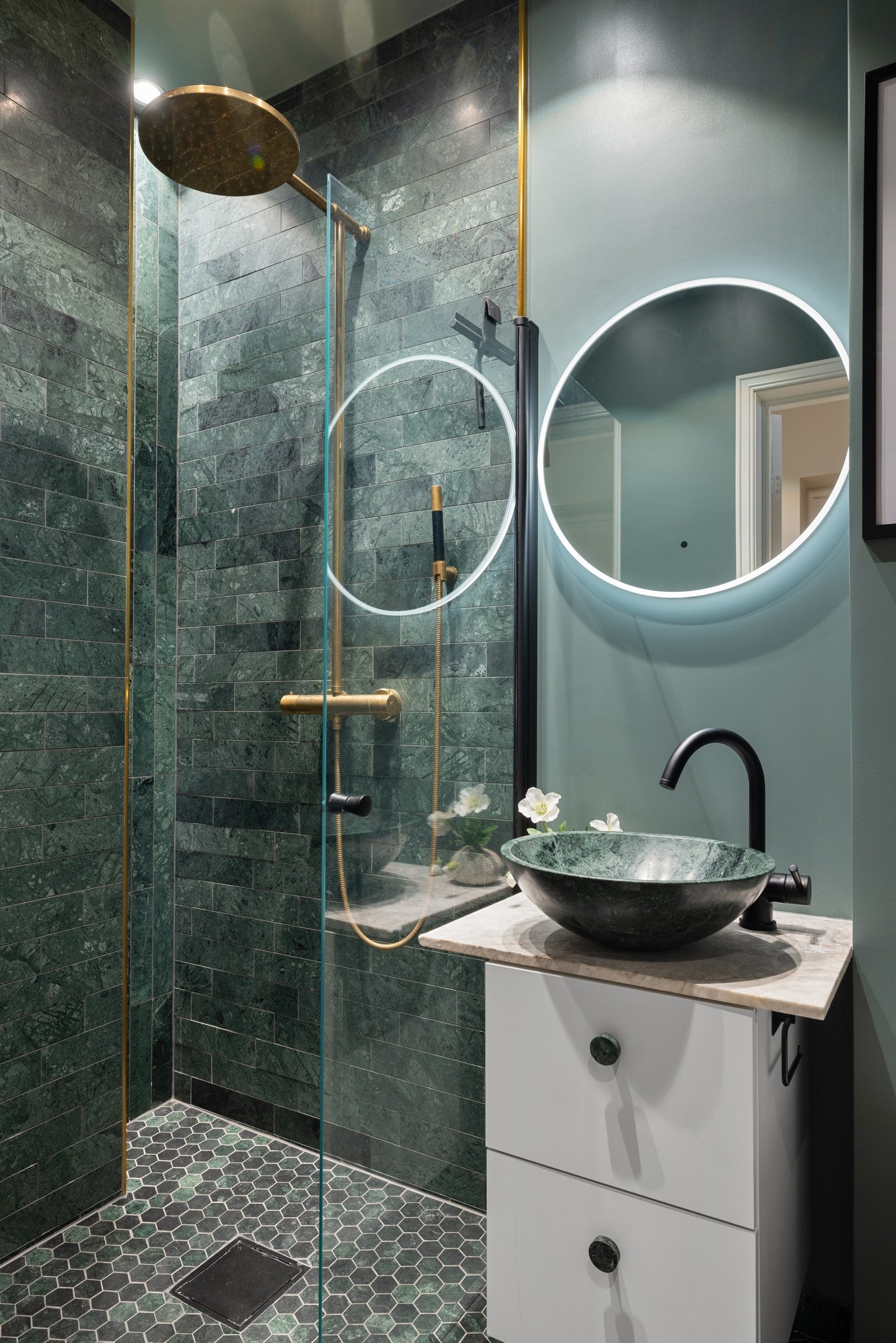 Rommet er innredet med regnfallsdusj, vegghengt toalett grønn marmorvask og marmorinnredning har sirkulært speil med belysning Galleribilde