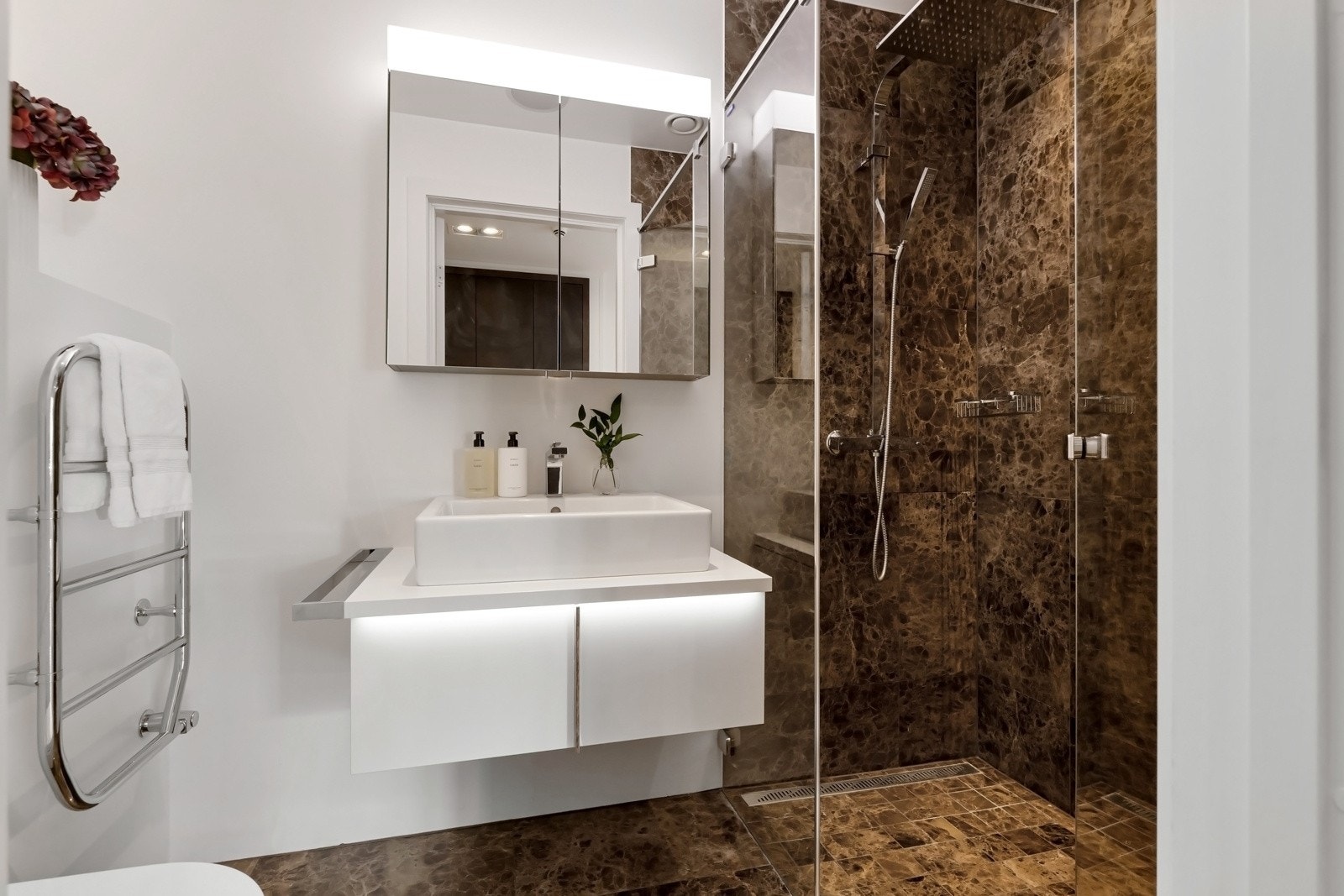 Badet med inngang fra hallen har samme lekre, brunmarmorerte gulvfliser som i hallen, gulvvarme, downlights og integrerte høyttalere i himlingen. Galleribilde