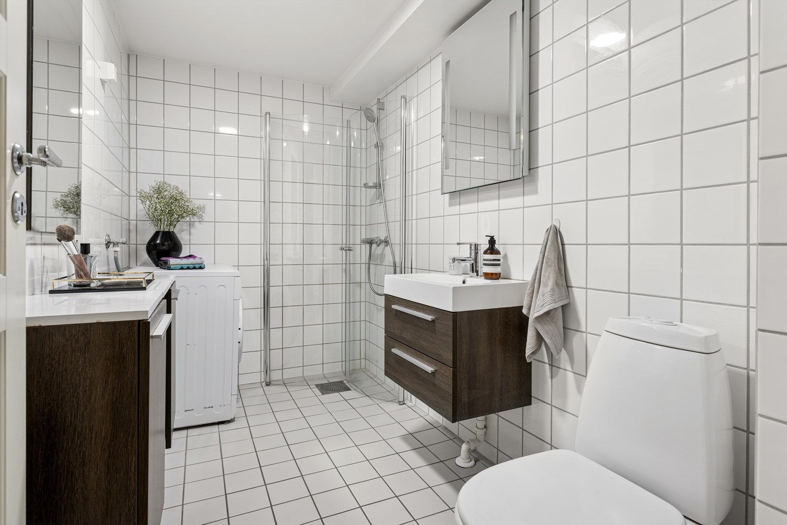 Pent flislagt bad med varmekabler, downlights i himling og opplegg for vaskemaskin. Badet består av frittstående wc, servant med underskap, speil, veggskap og inn-/utadslående dusjdører Galleribilde