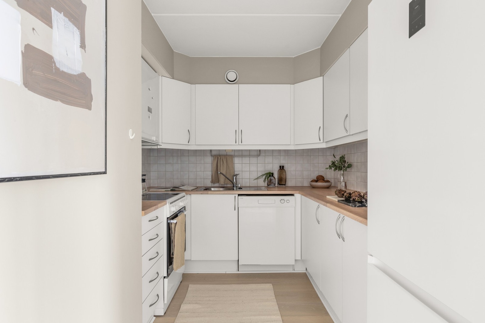 Kjøkkenet har en praktisk løsning med god skap- og benkeplass. Tidløs innredning fra byggeåret med hvite glatte fronter og ny laminat benkeplate fra 2025. Galleribilde