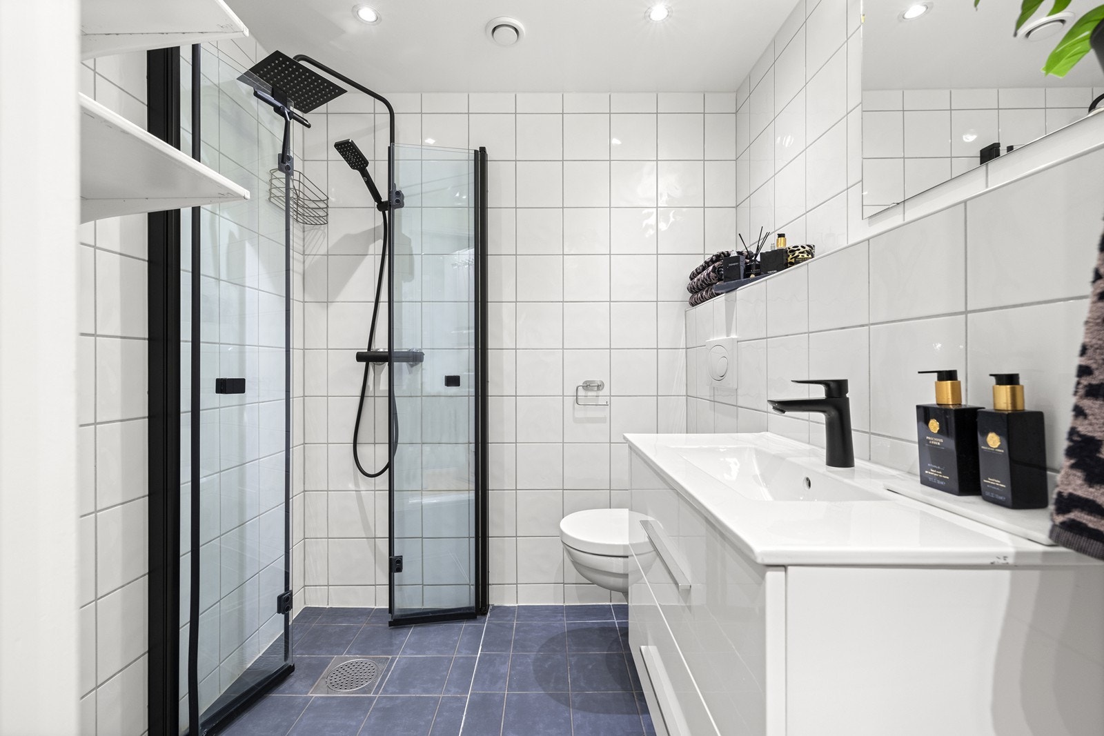 Baderom med flislagte gulv og vegger. Badet er utstyrt med vegghengt toalett, servant med skuffer og dusjnisje med innfellbare glassdører. Galleribilde