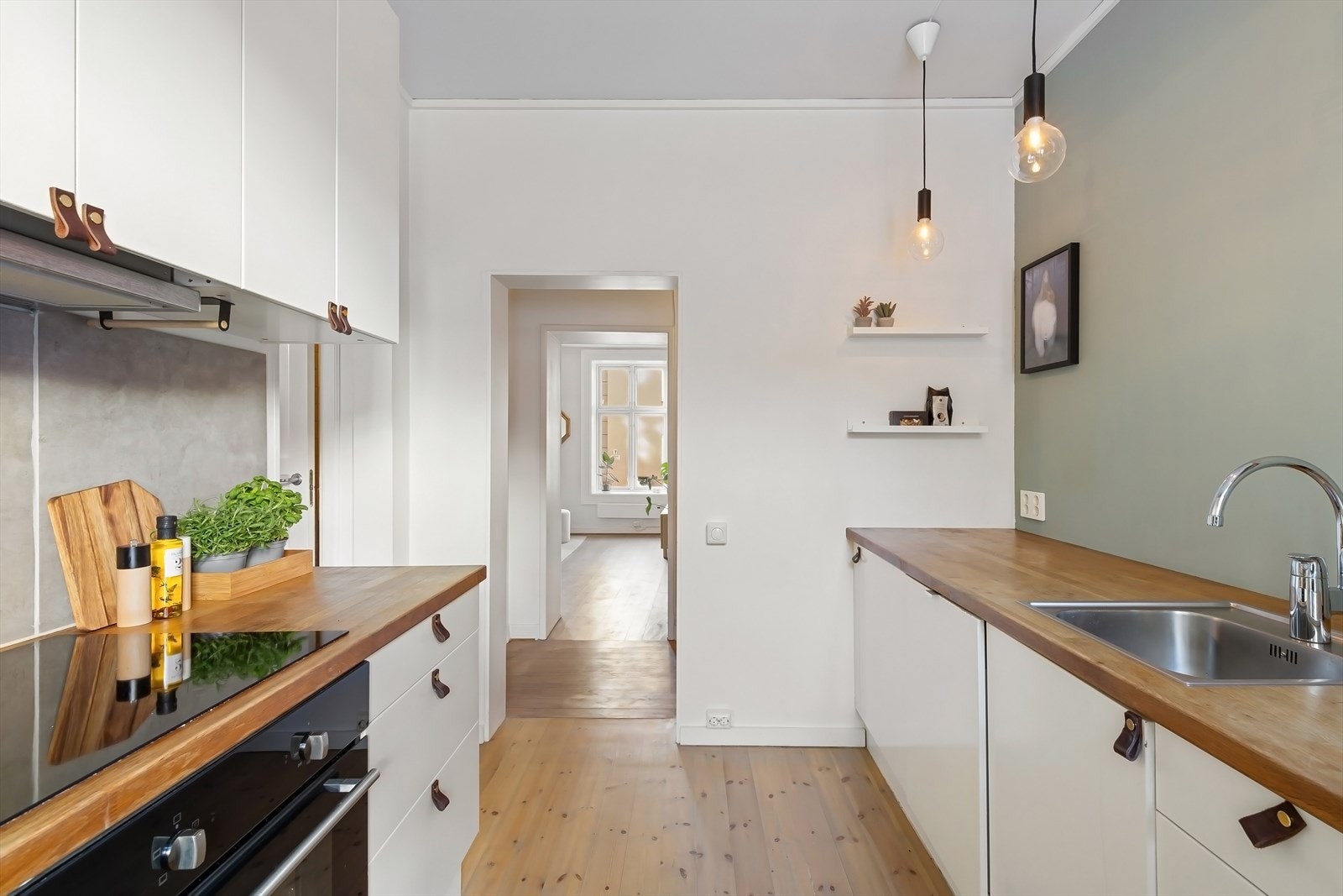 Moderne kjøkken med hvite, glatte fronter og heltre benkeplate (slipt og oljet i februar 2025). Integrerte hvitevarer med induksjonstopp, stekeovn, oppvaskmaskin og kjøl/frys. Galleribilde