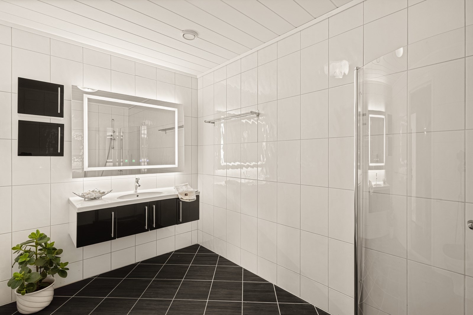 Badet har keramiske fliser på vegger med varmekabler og smartpanel i himling. Badet har servant med møblement, speil m/belysning, vegghengt toalett og innfellbare dusjdører. Galleribilde