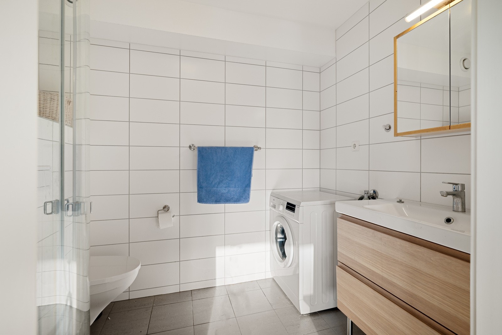 Flislagt bad med gulvvarme. Utstyrt med innfellbare dusjdører, servantskap, veggmontert wc og vaskemaskin. Galleribilde