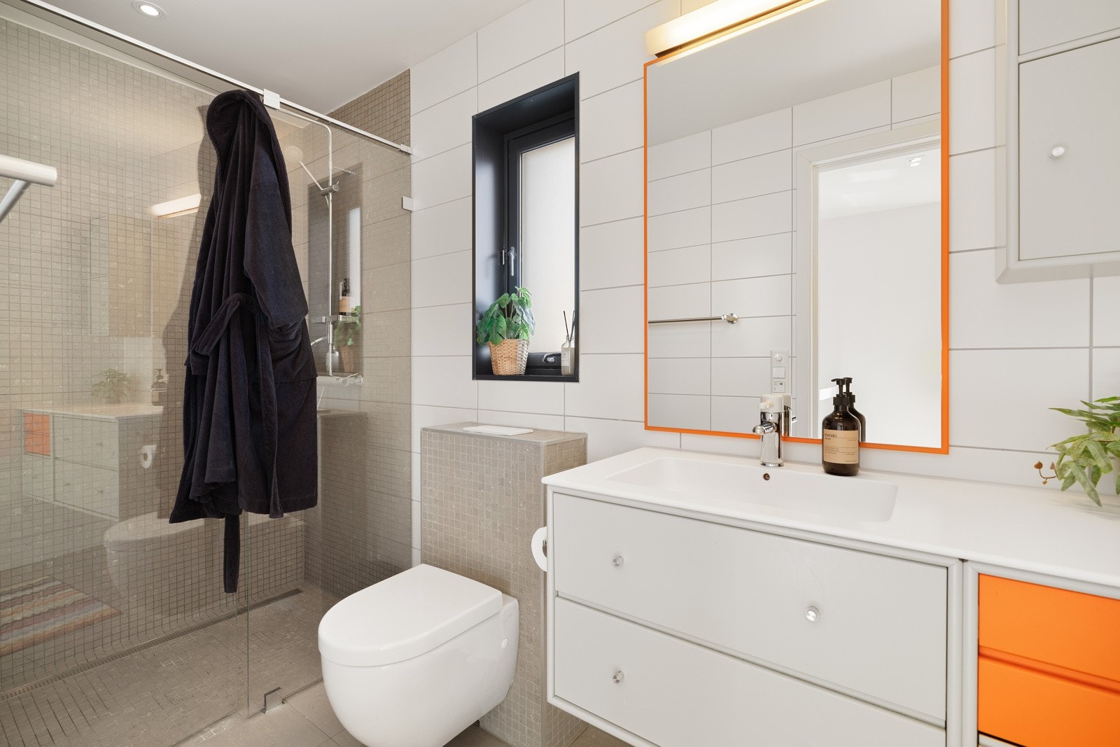 Fint bad med flis på gulv og vegger. Utstyrt med innfellbare dusjdører, servantskap og veggmontert wc. Galleribilde