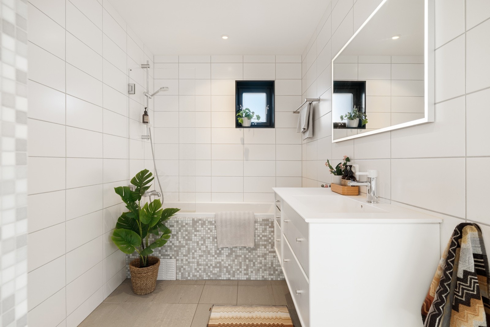 Stilrent, flislagt bad. Utstyrt med badekar, innfellbar dusjdør, servantskap og veggmontert wc. Alle badene har en baderomsinnredning fra Montana. Galleribilde