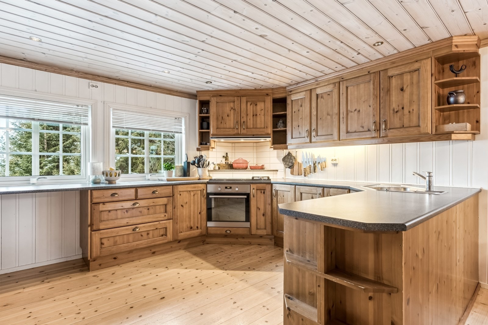 Oppvaskkum nedfelt i laminat benkeplate, integrert platetopp med to gassbluss og komfyr, frittstående oppvaskmaskin og kjøl-/fryseskap. Galleribilde