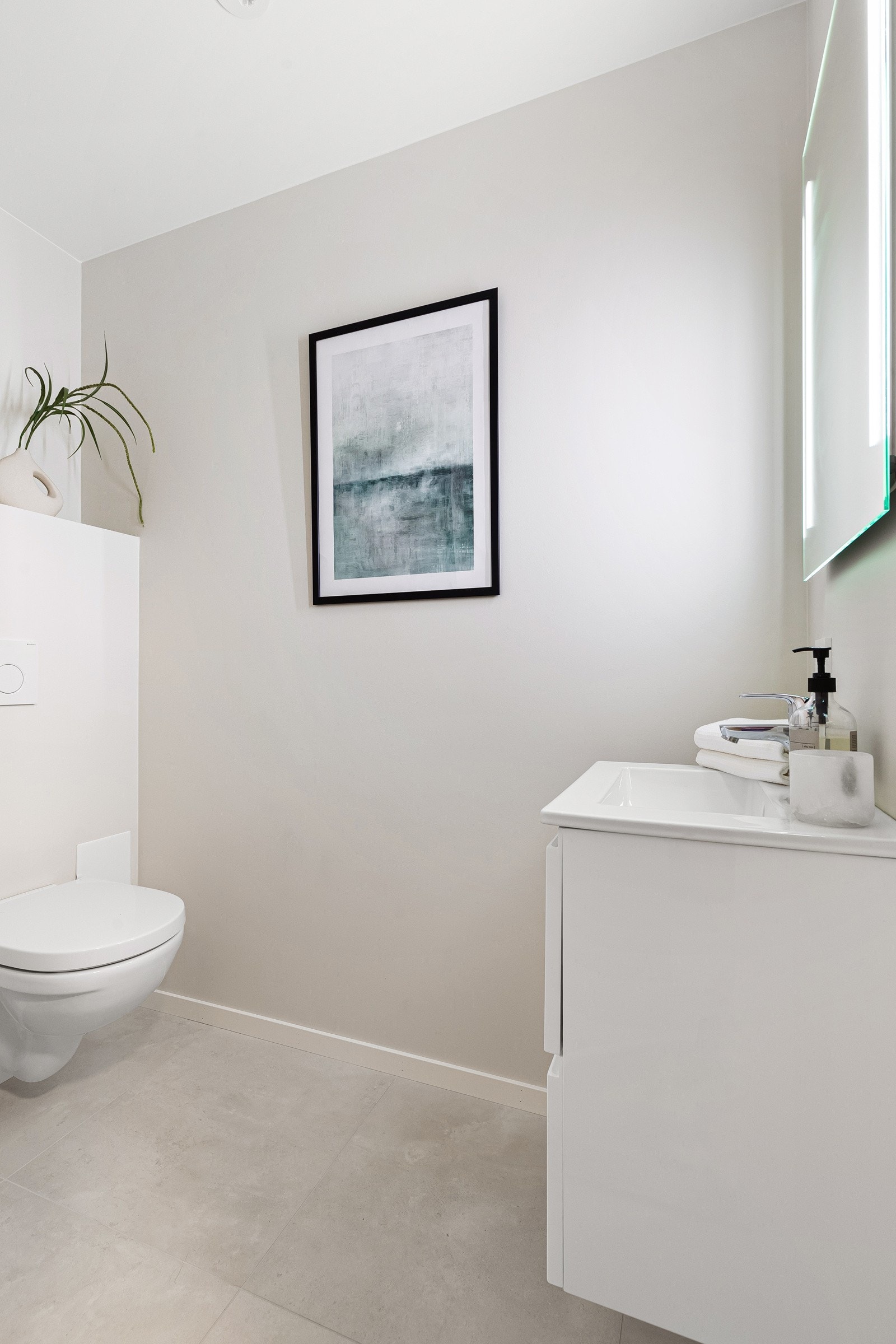 Toalettrom tilknyttet entré med servant med skap, vegghengt toalett og speil med belysning. Galleribilde