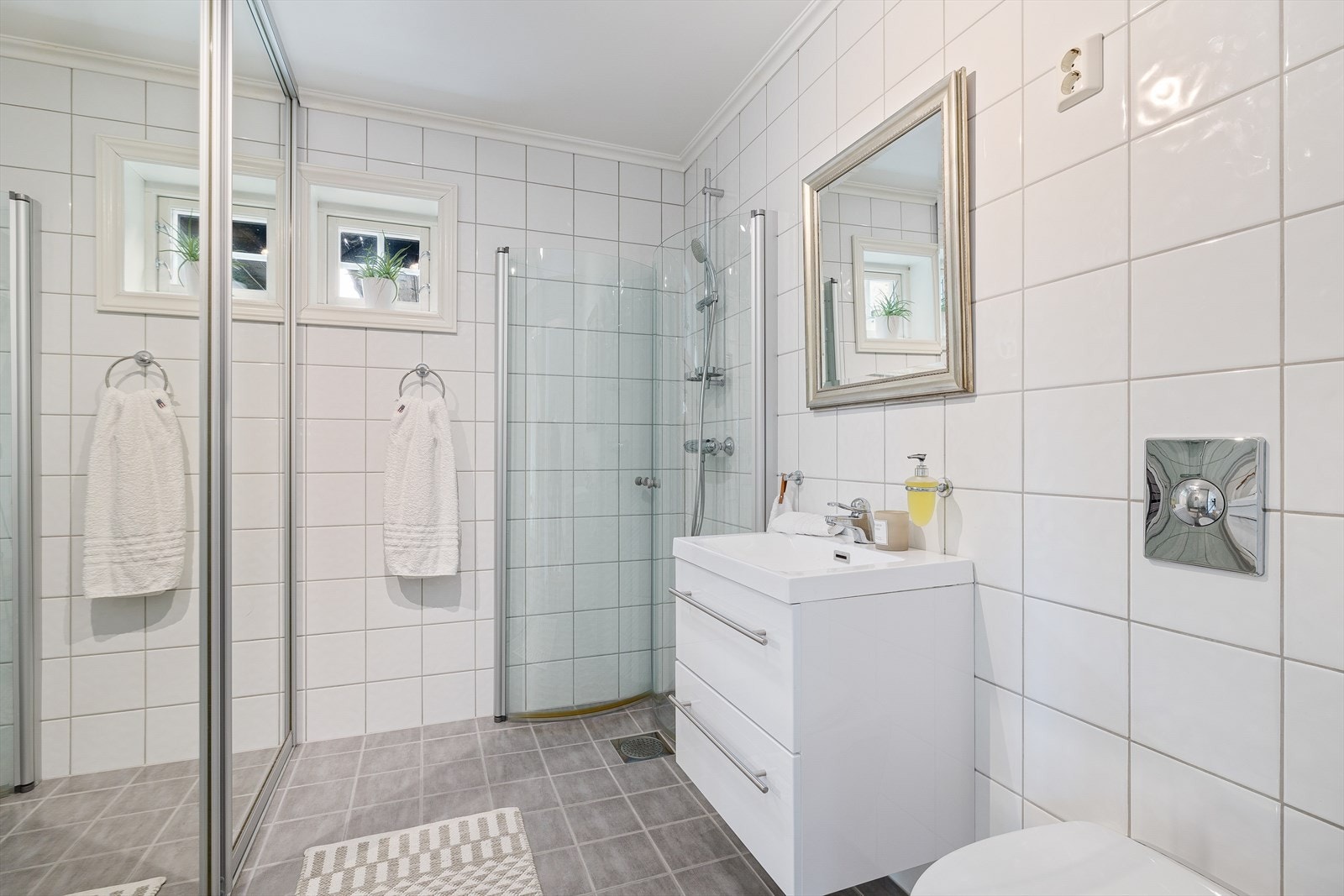 Bad/Vaskerom innredet med nedfelt servant, veggmontert toalett, dusjhjørne, speil, skyllekum, hylle og opplegg til vaskemaskin Galleribilde