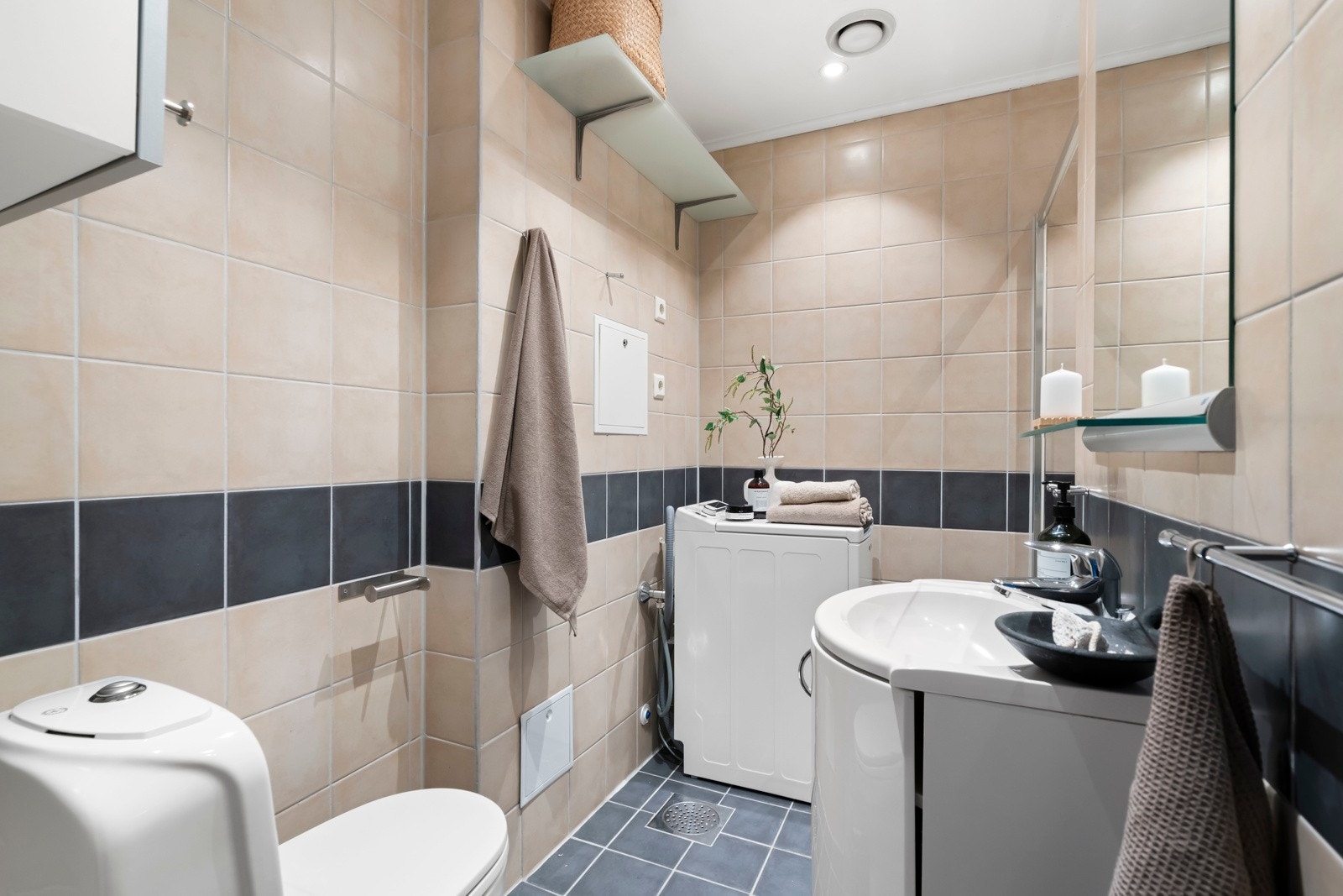 Eldre flislagt baderom med opplegg for vaskemaskin. Frittstående toalett og skap med oppbevaringsplass. Galleribilde