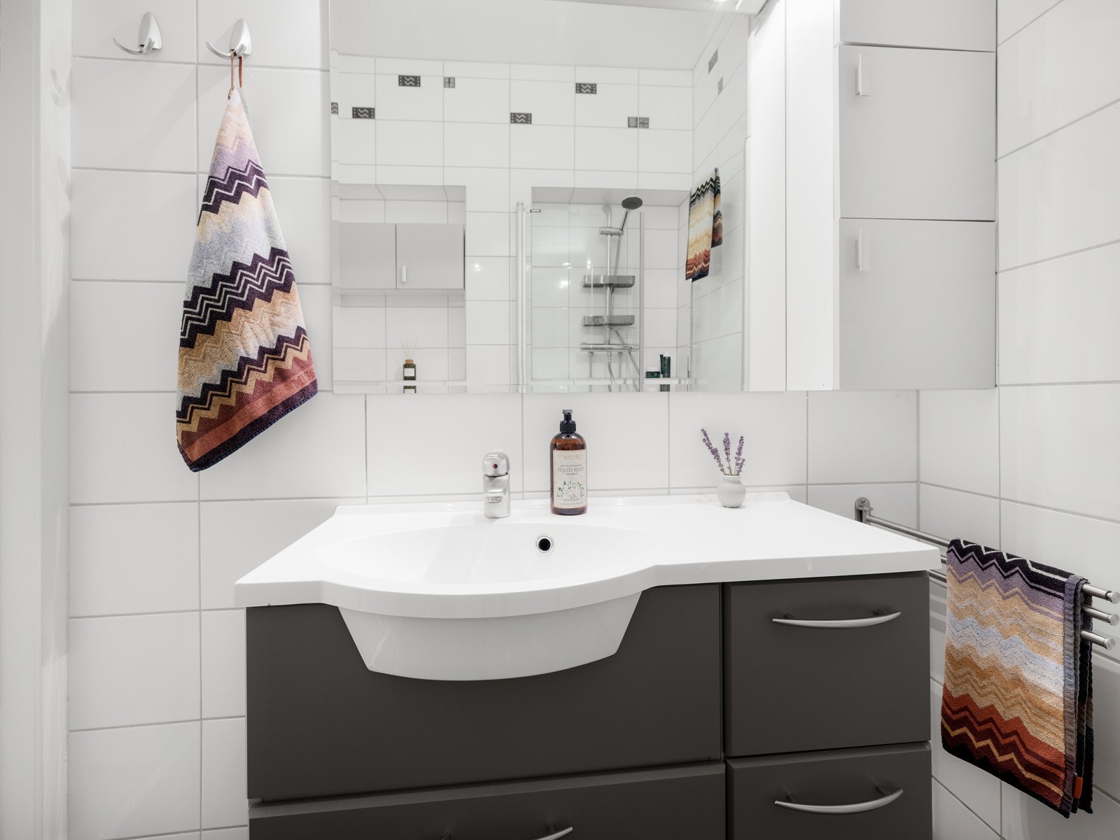 Badet inneholder servant, speil med stikkontakt, vegghengt toalett og dusj med innfellbare dører av glass Galleribilde