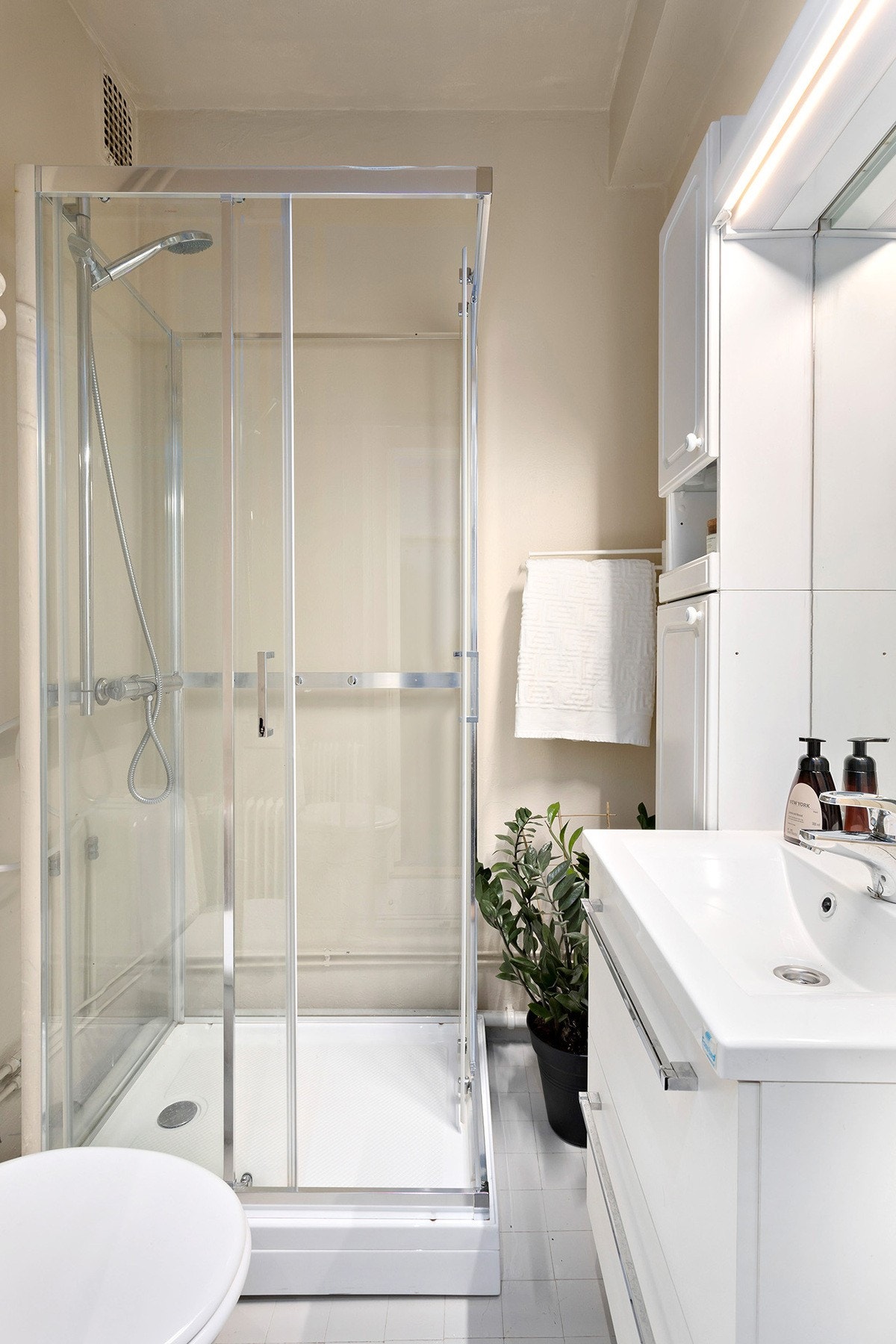 Bad med toalett, dusjkabinett i herdet glass, speil med overliggende belysning,
baderomsinnredning med malte/finerte fronter og heldekkende servant. Galleribilde