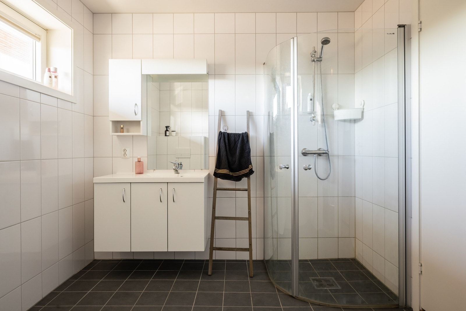 Badet er innredet med vegghengt toalett, opplegg for vaskemaskin, servant med innredning og dusj med foldedører. Galleribilde